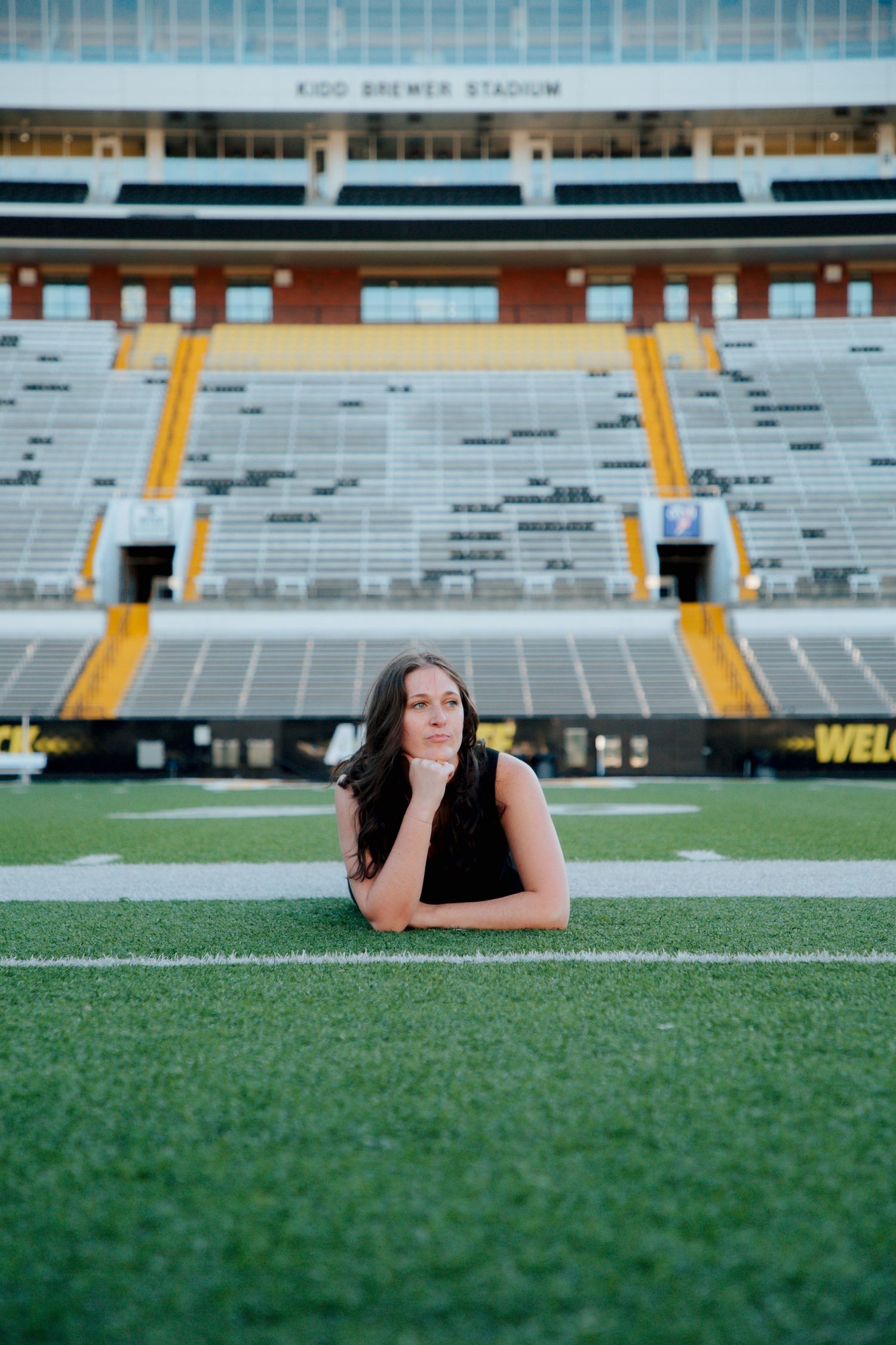 Young woman in black dress posing thoughtfully on Kidd Brewer Stadium football field at App State.
