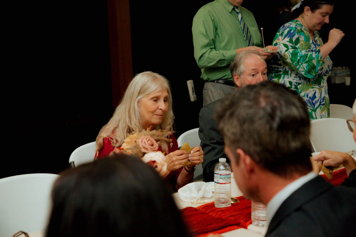 Wedding guests enjoy conversation and refreshments at a reception dinner table.