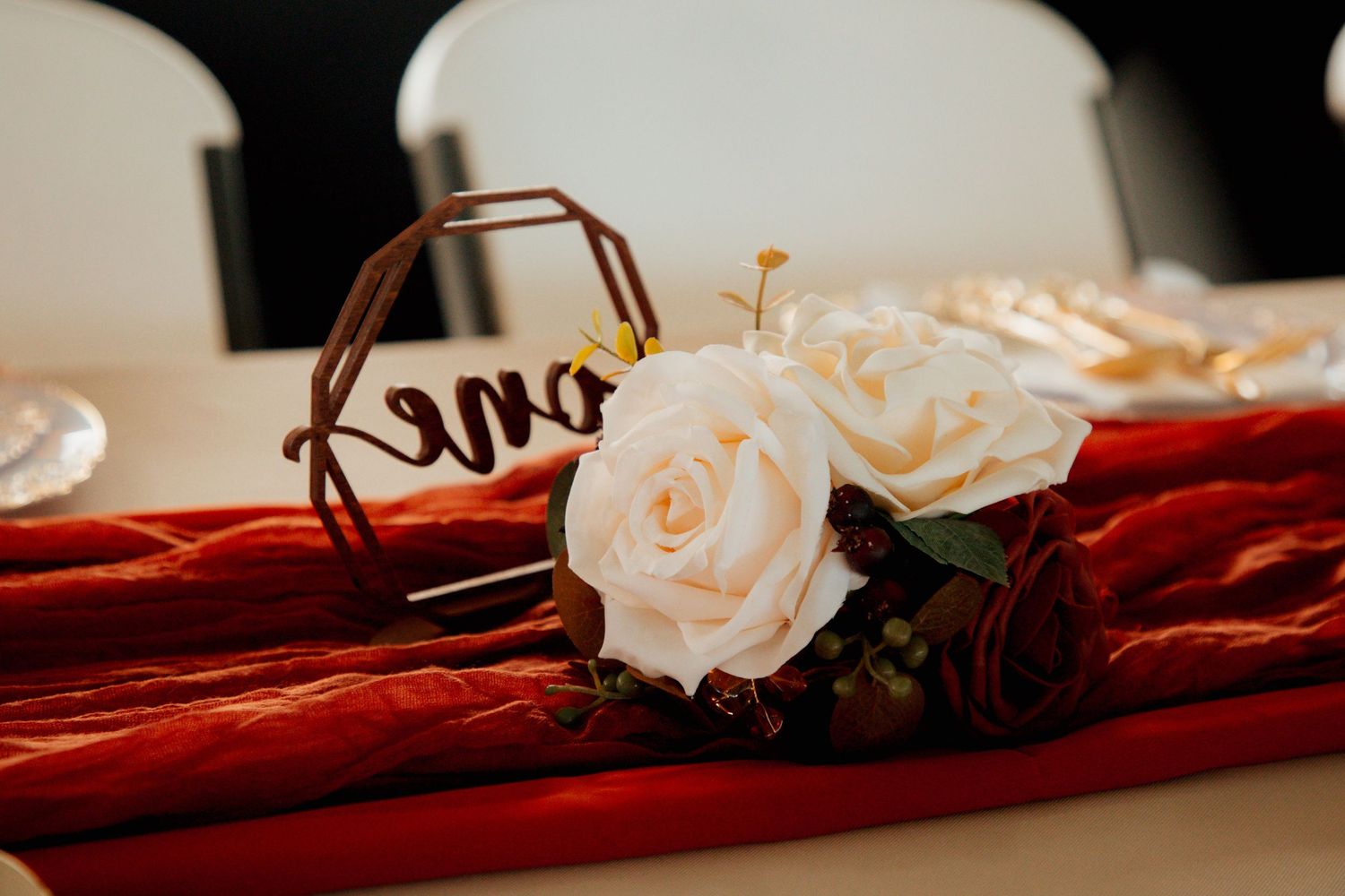 Close-up of red velvet table runner with white roses and gold name sign decoration.