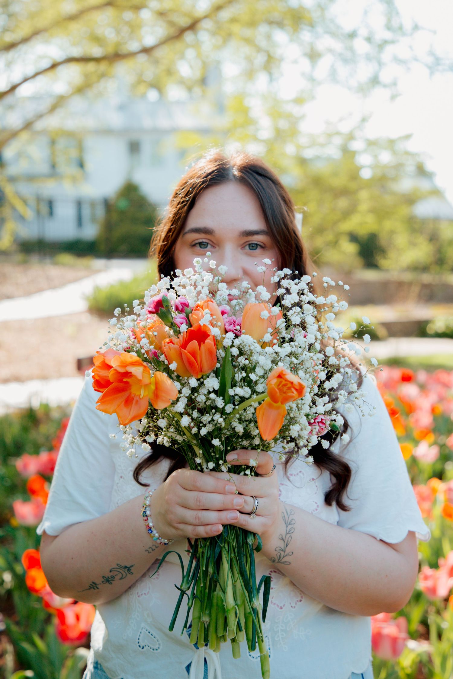 Woman holds large bouquet of orange tulips and white baby's breath flowers up to her face outdoors.