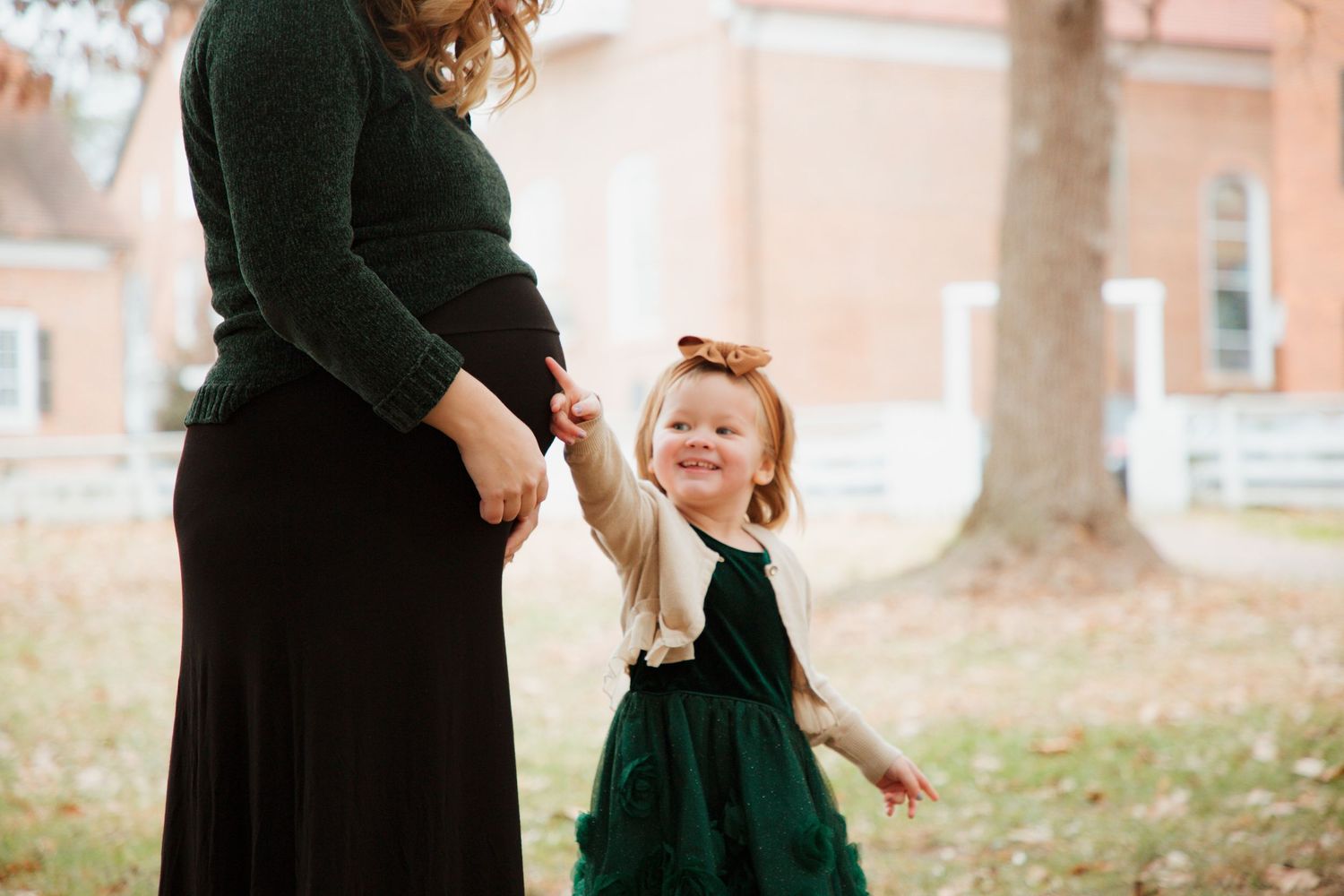 Happy toddler girl in green dress holding pregnant mothers hand outdoors in autumn.