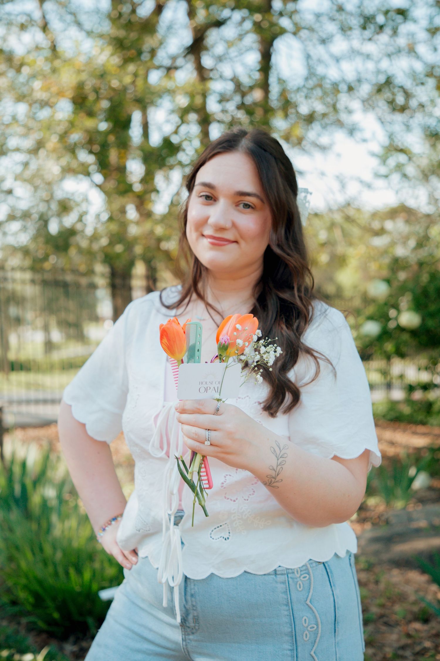 Brunette woman smiles softly holding orange tulips and baby's breath bouquet in green garden.