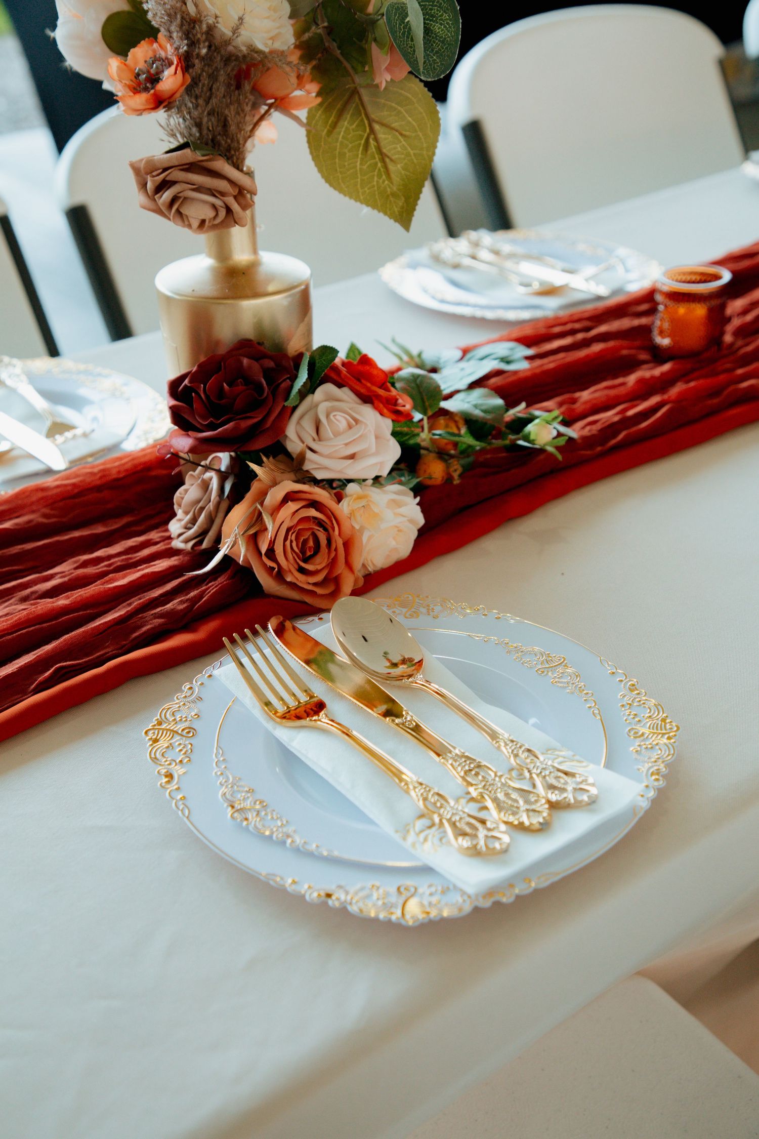 Elegant wedding table setting with gold cutlery, white plates, and red rose floral runner.