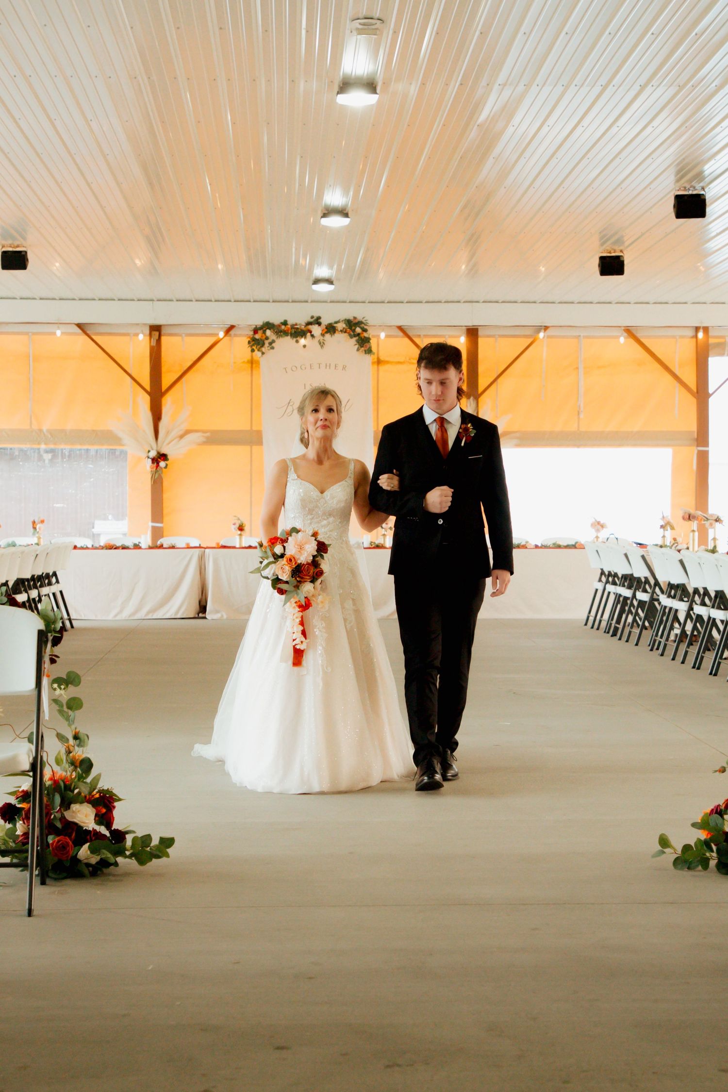 A bride and groom walk down the aisle together in a rustic barn wedding venue decorated with floral arrangements.