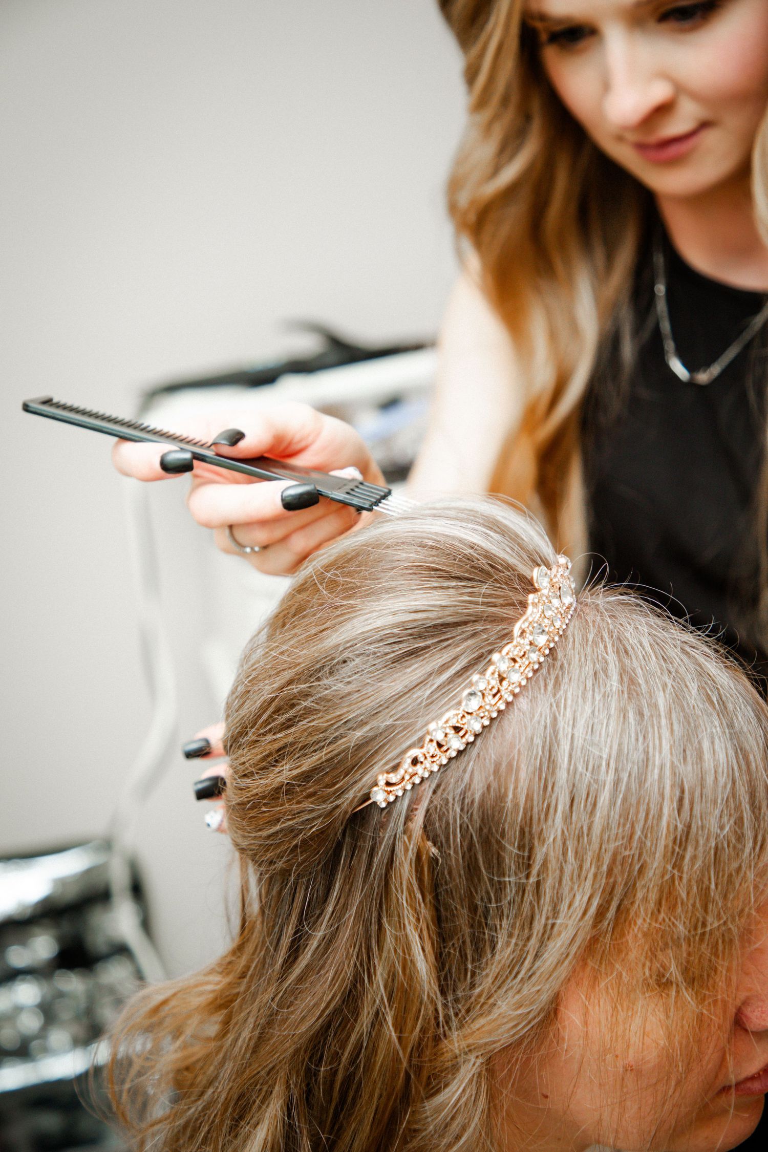 Hair stylist using flat iron to style bride's hair adorned with a rose gold tiara headpiece.