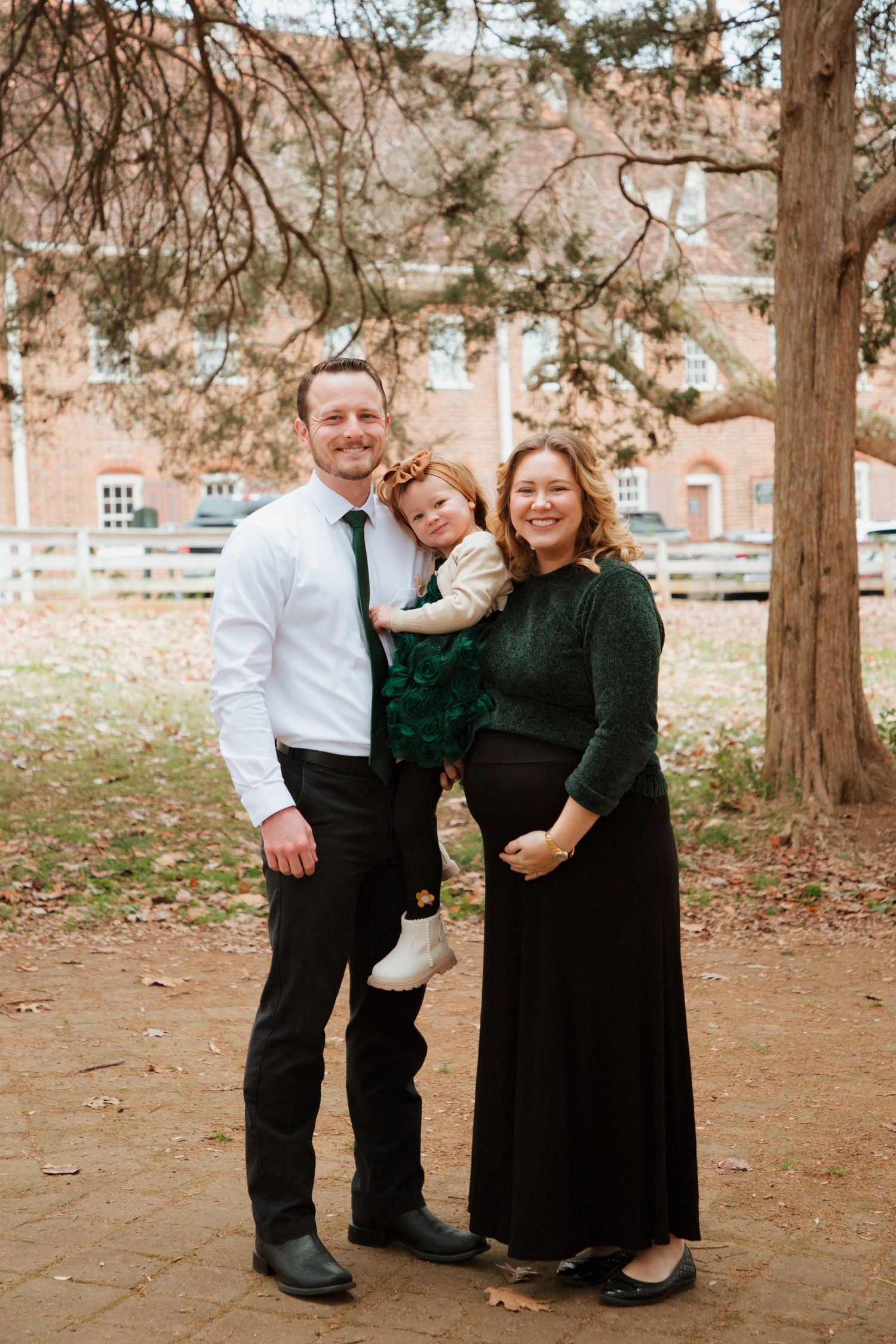 Happy family with pregnant mother, father, and toddler posing outdoors near brick building.