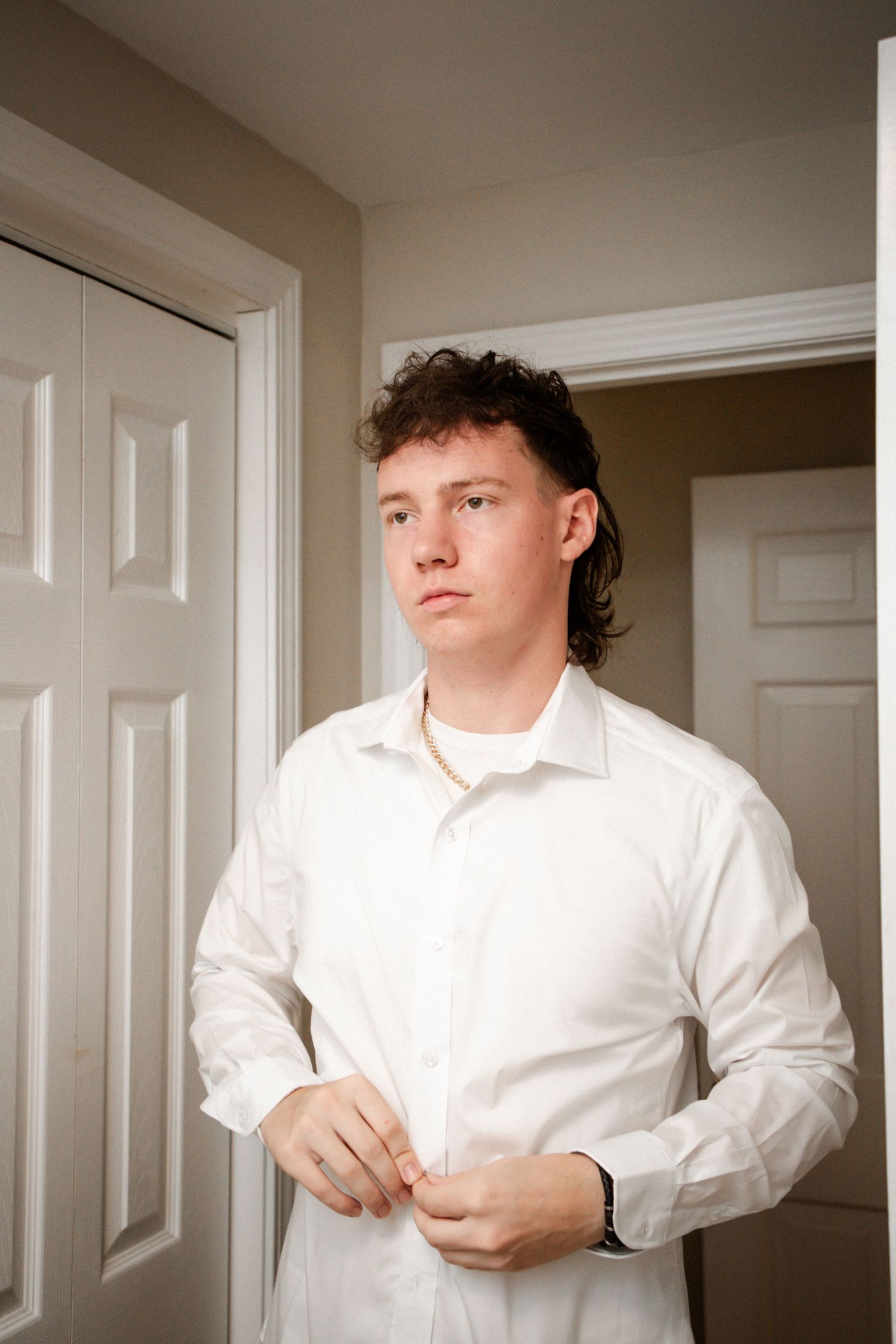Young man in white dress shirt buttoning up while getting ready for a wedding.
