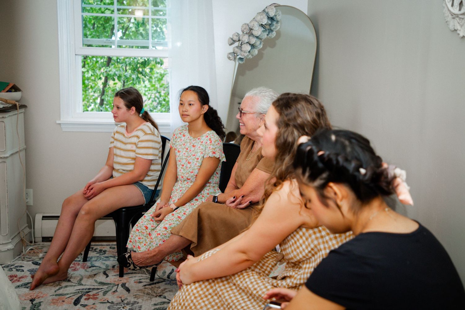 Group of women sitting in a row during a wedding preparation gathering indoors.