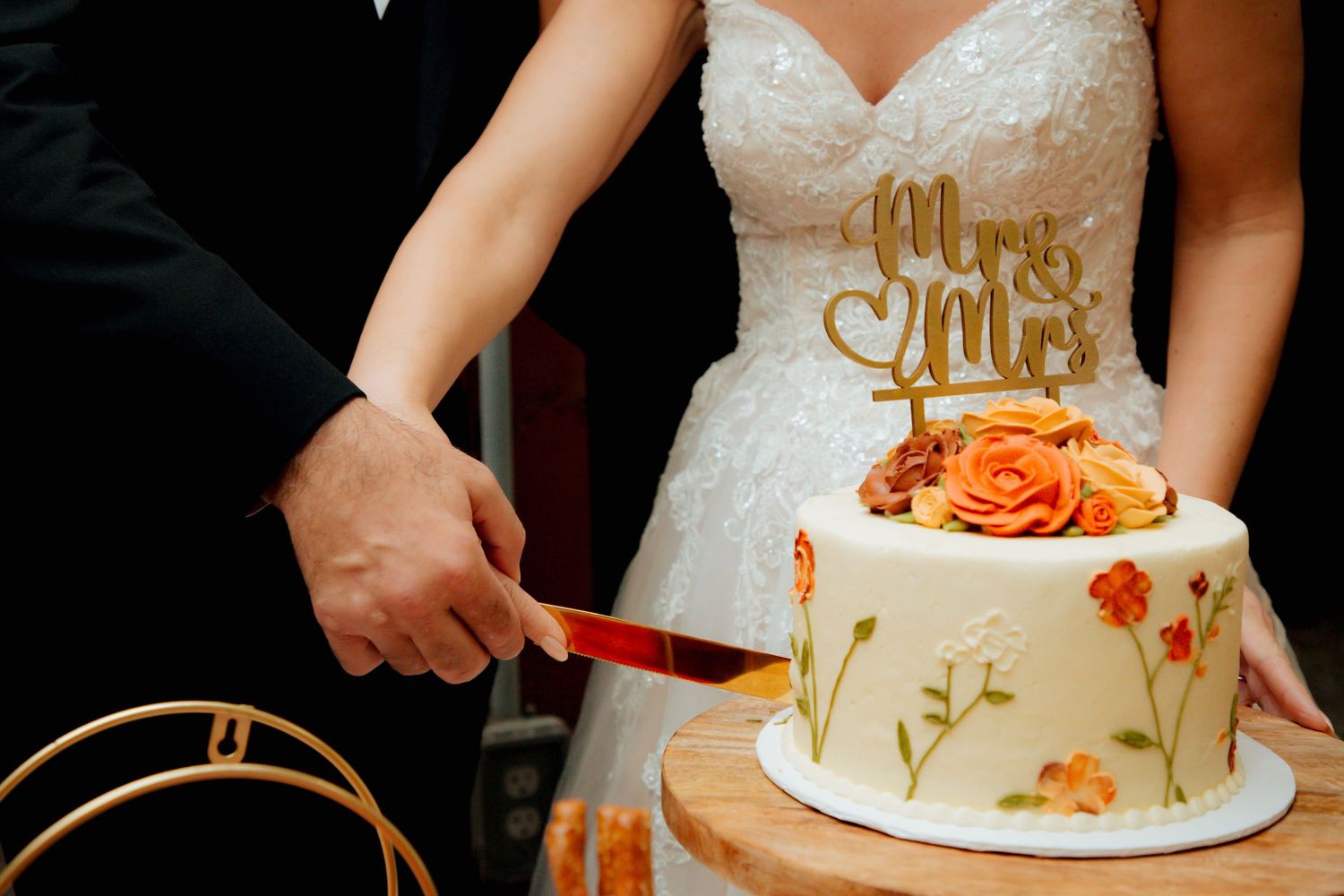 Bride and groom slice their elegant white wedding cake decorated with orange flowers.