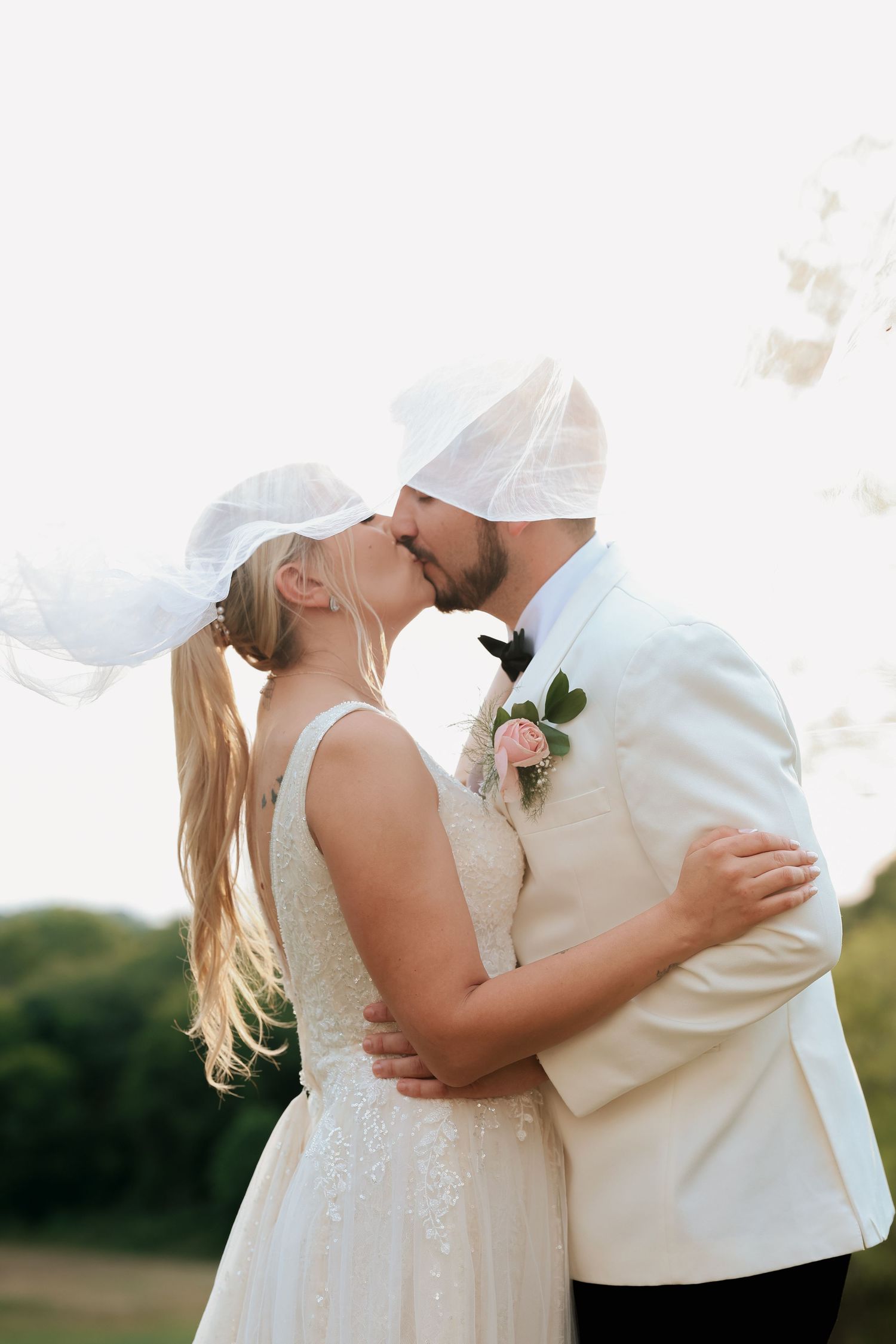 Bride and groom sharing a kiss as the veil billows in the wind during an outdoor wedding portrait.