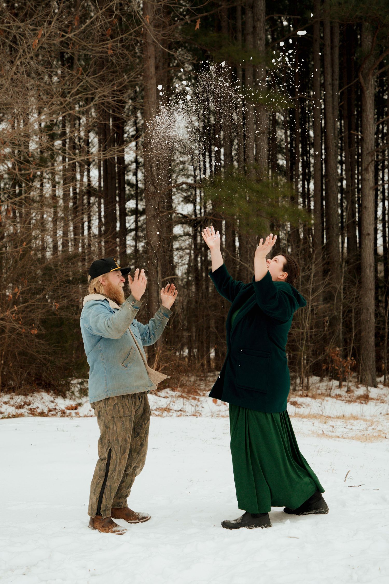 Couple joyfully tossing snow in the air in a snowy forest clearing in winter.