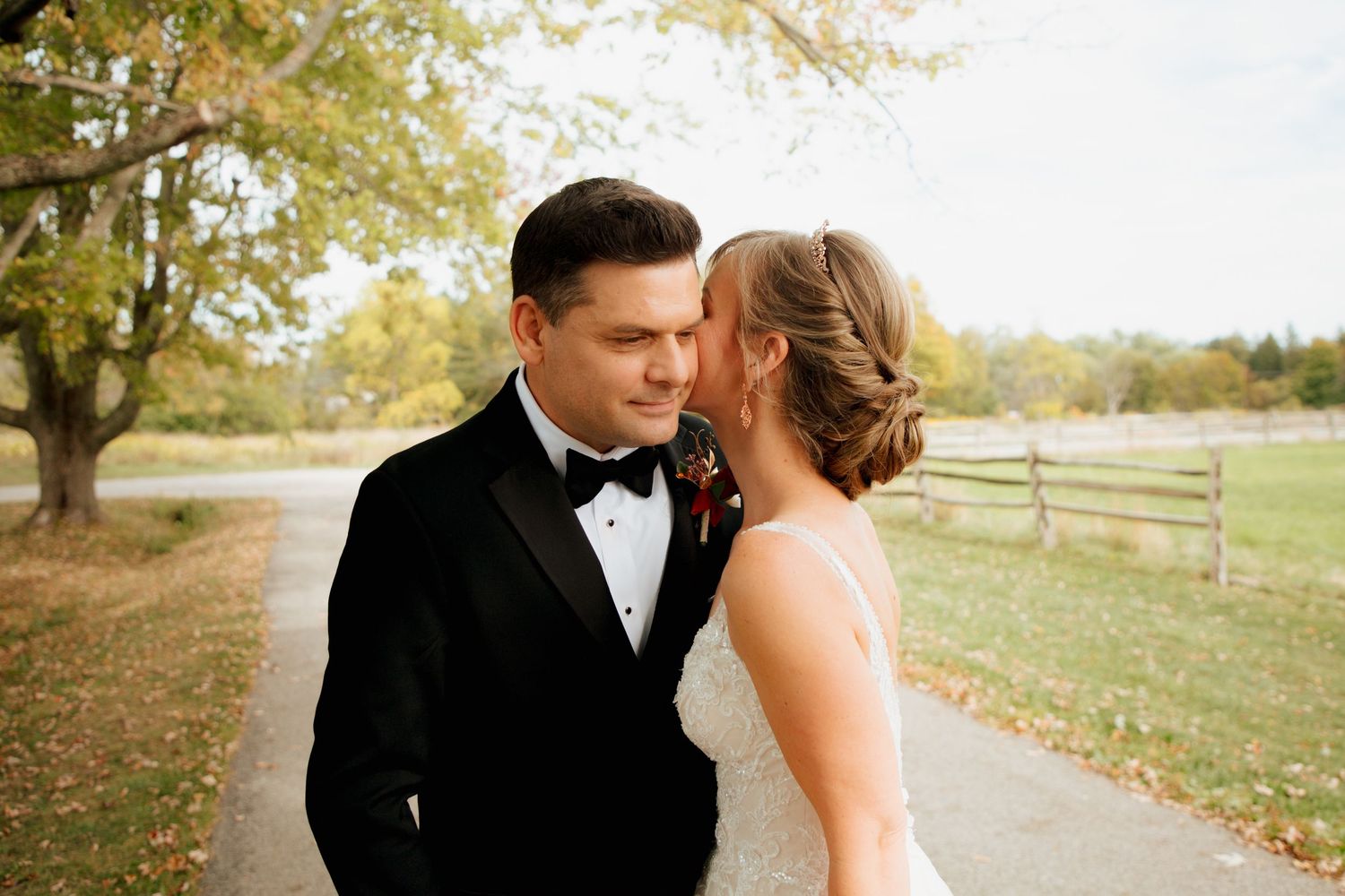 Bride whispering to groom in black tuxedo during romantic outdoor fall wedding portraits.