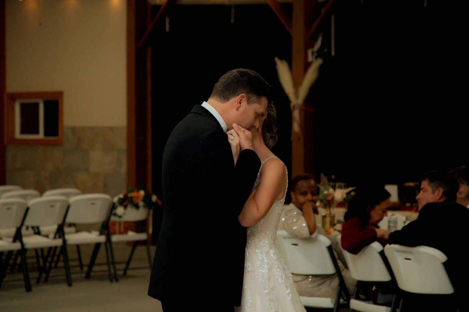 Groom tenderly kisses bride's hand during their first dance at a rustic barn wedding reception.
