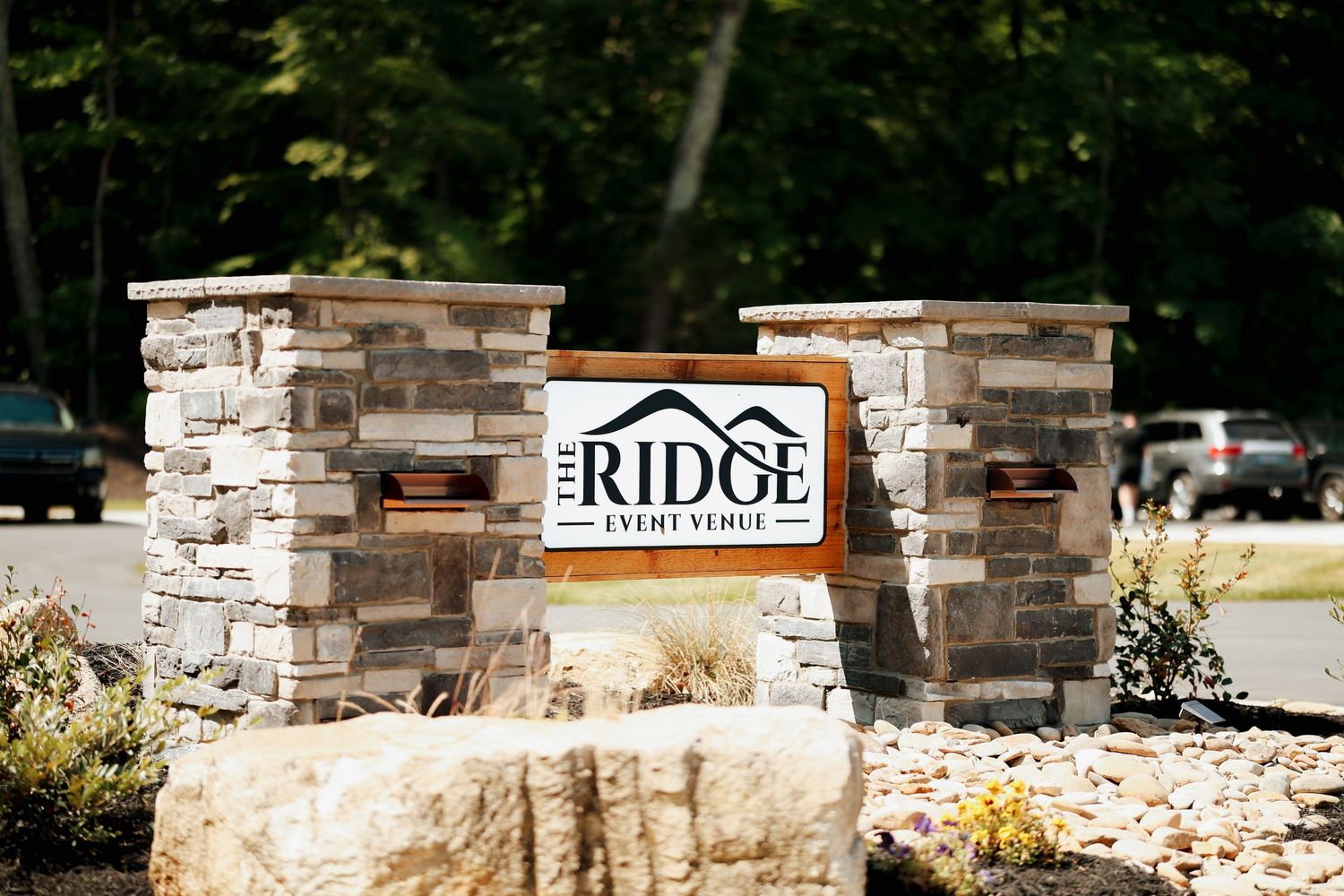 Stone entrance sign for The Ridge Event Venue surrounded by lush green trees.