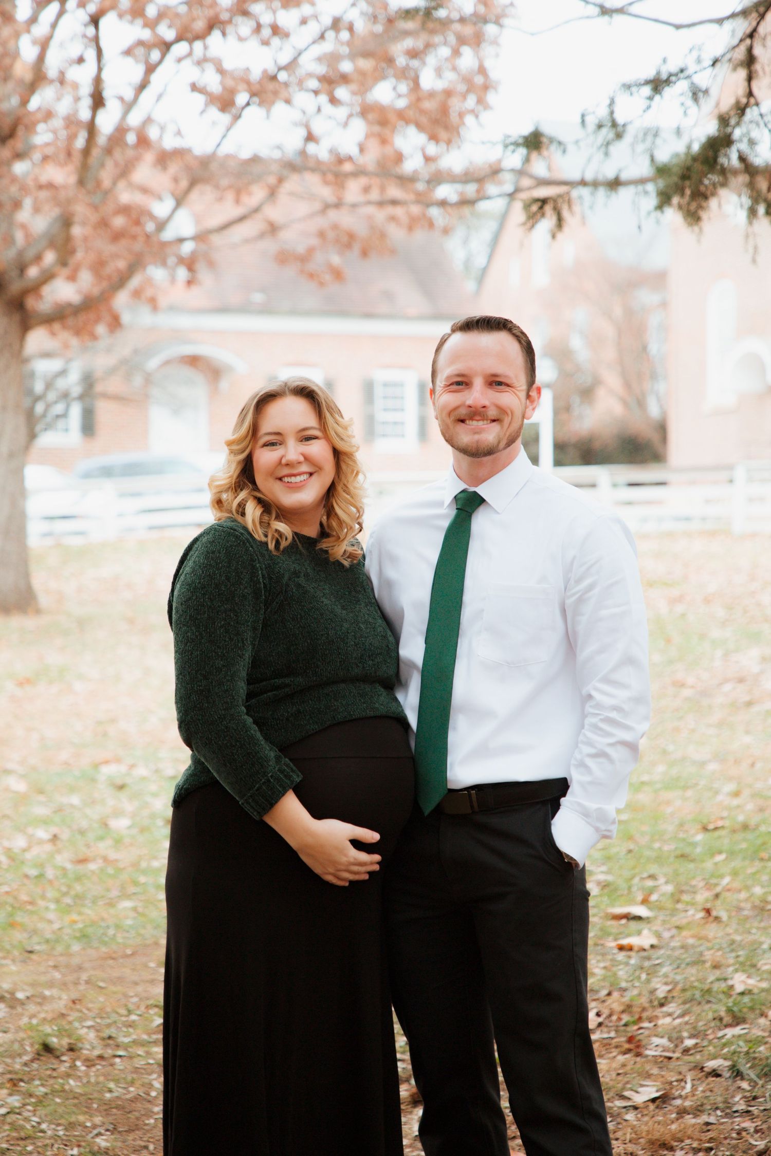 Smiling pregnant couple in coordinating green outfits posing together in autumn park.