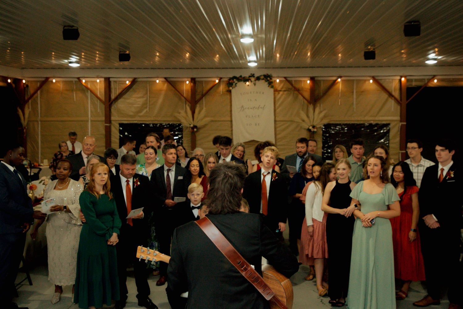 Musician performing guitar for wedding guests gathered at rustic barn reception.