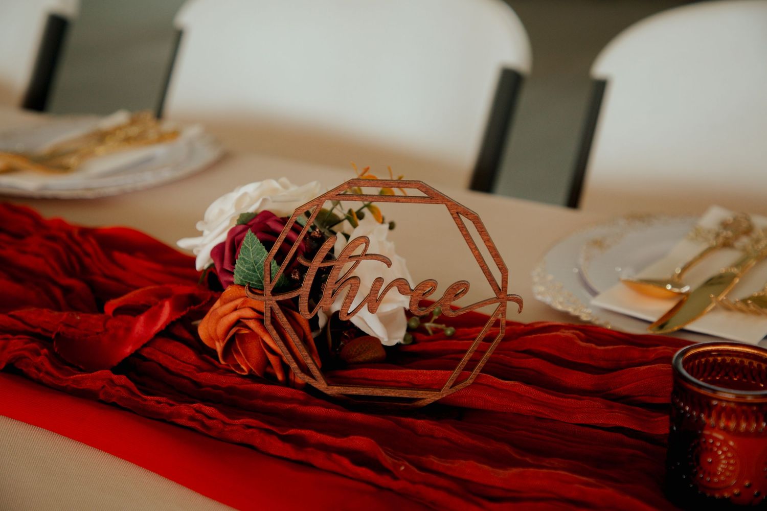Elegant wedding table centerpiece with geometric copper number three sign, red velvet runner, and colorful floral arrangement.