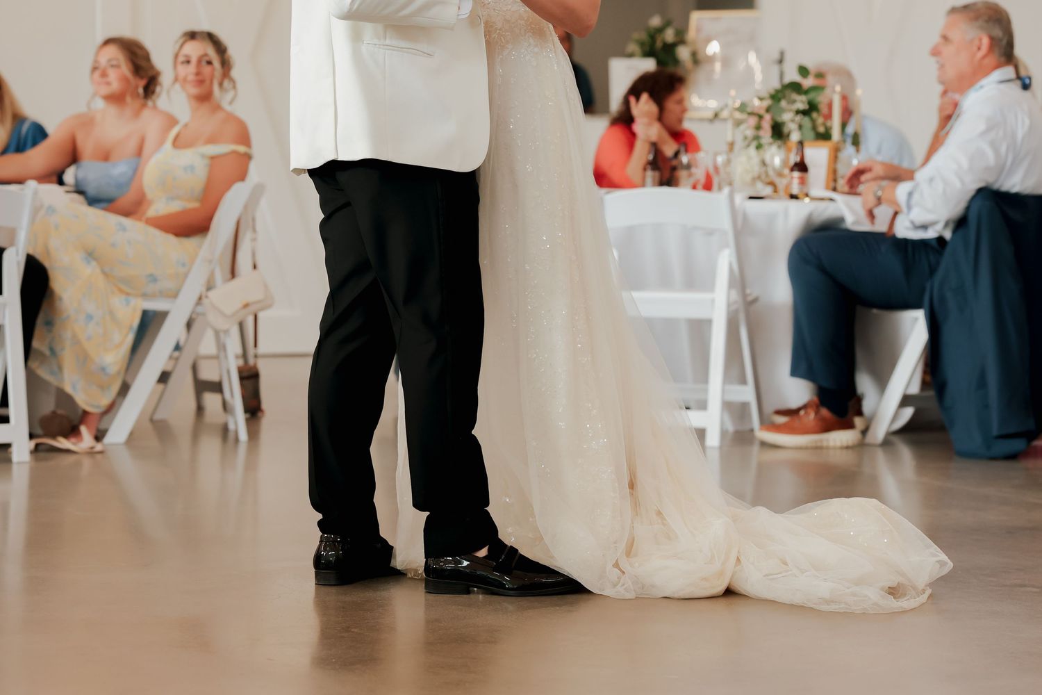 Bride and groom share intimate first dance, wedding dress train flowing on reception floor.