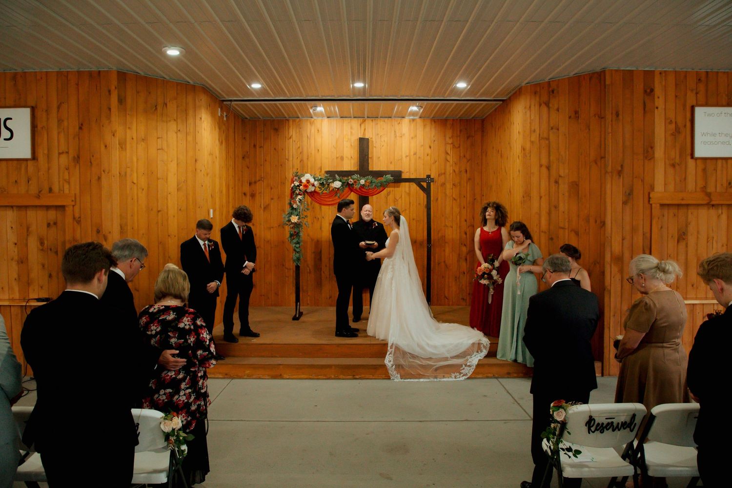 A wide-angle view of a rustic wood-paneled wedding ceremony with guests gathered around the altar.