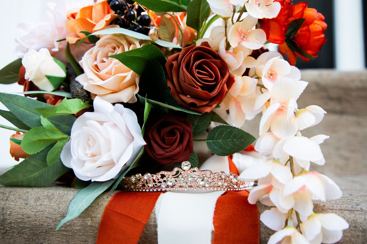 Bridal bouquet featuring terracotta, blush, burgundy roses with a rose gold tiara and orange ribbon wrap.