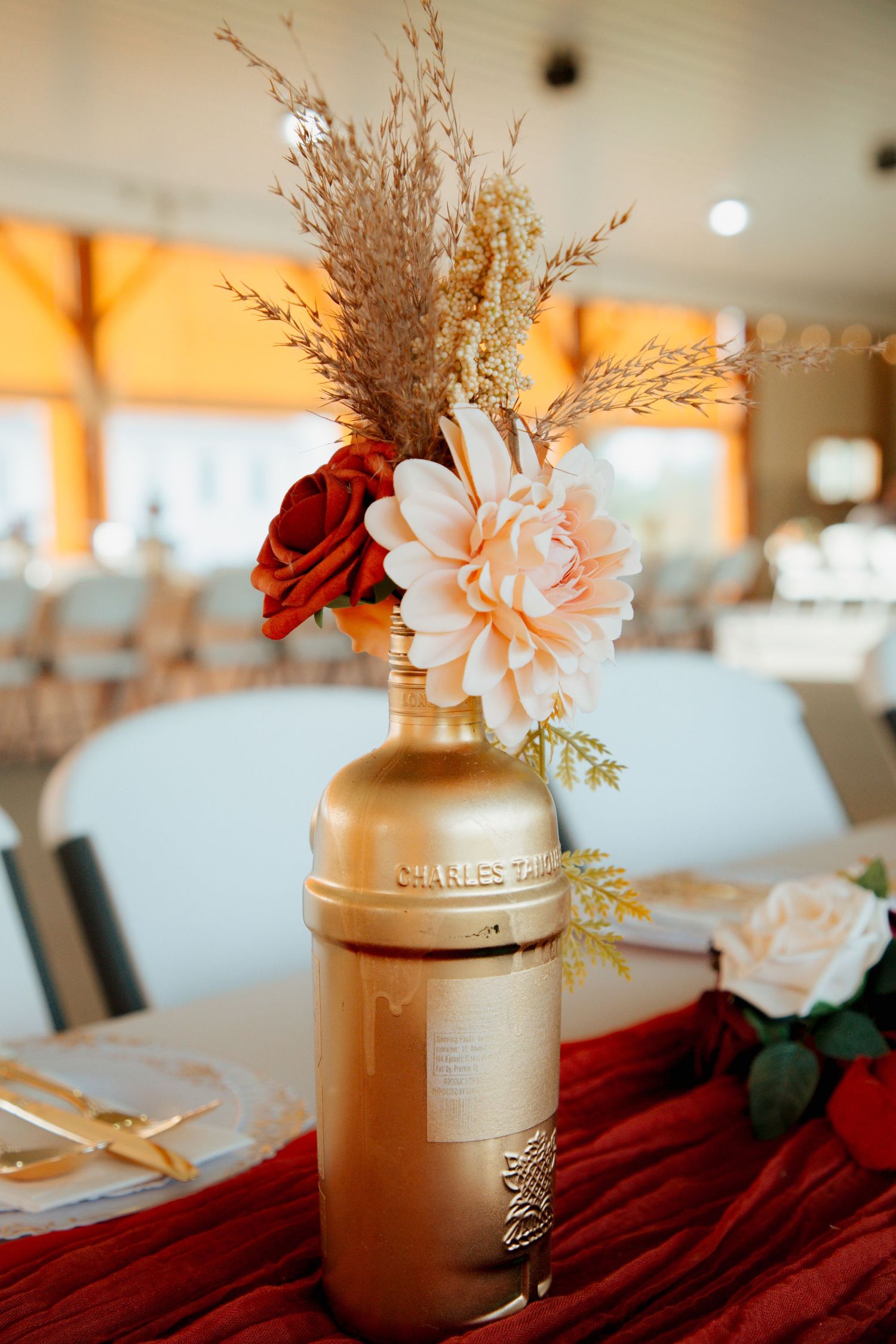 Gold-painted Charles Tanqueray bottle vase with dahlia and red roses as centerpiece.
