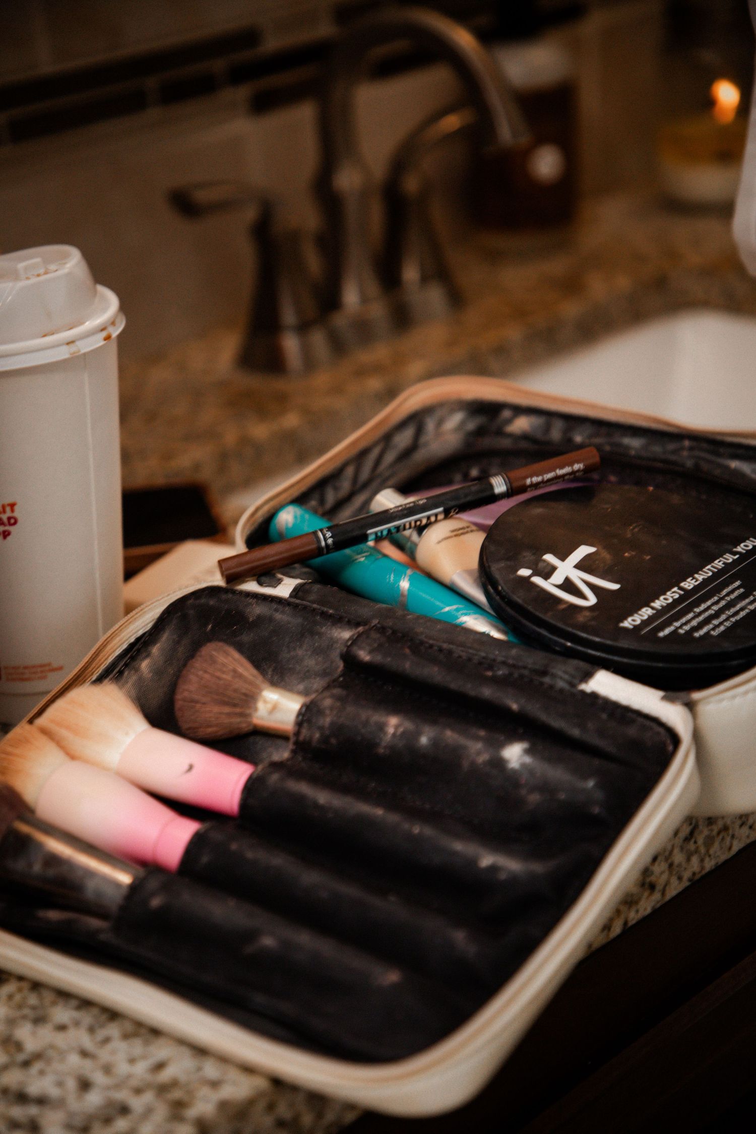 Open makeup bag with brushes and cosmetics on a bathroom counter near sink.