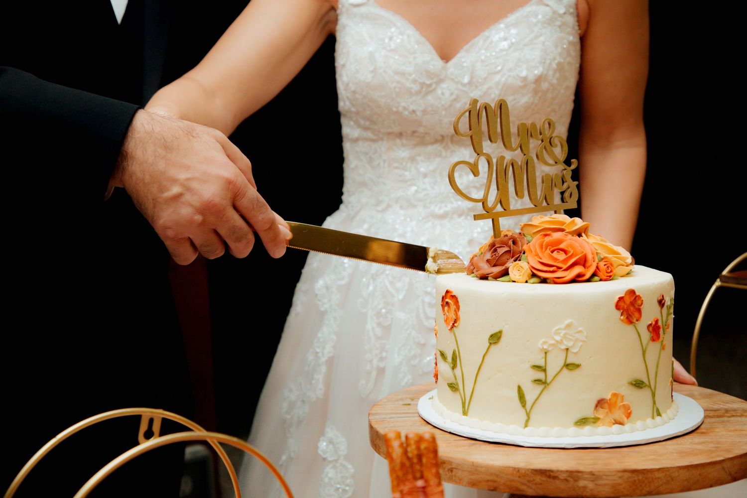 Close-up of bride and groom cutting a white floral wedding cake with Mr & Mrs topper.