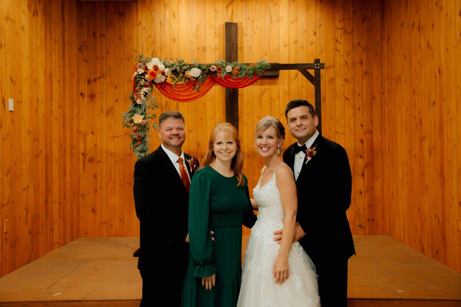 Wedding party of four posing before floral cross arch, bride in white gown with groom.