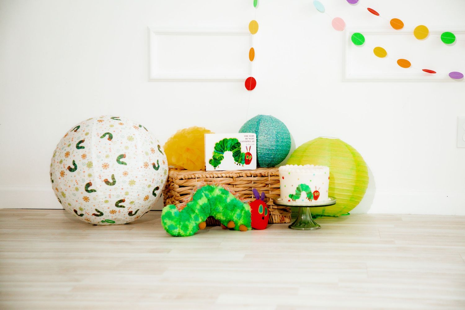Very Hungry Caterpillar themed party decorations with lanterns, book, and caterpillar toy in wicker basket.