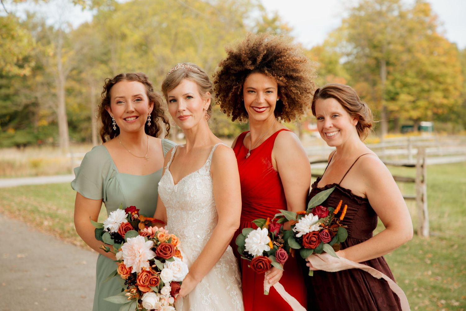 Bride and three bridesmaids holding fall bouquets outdoors in autumn.