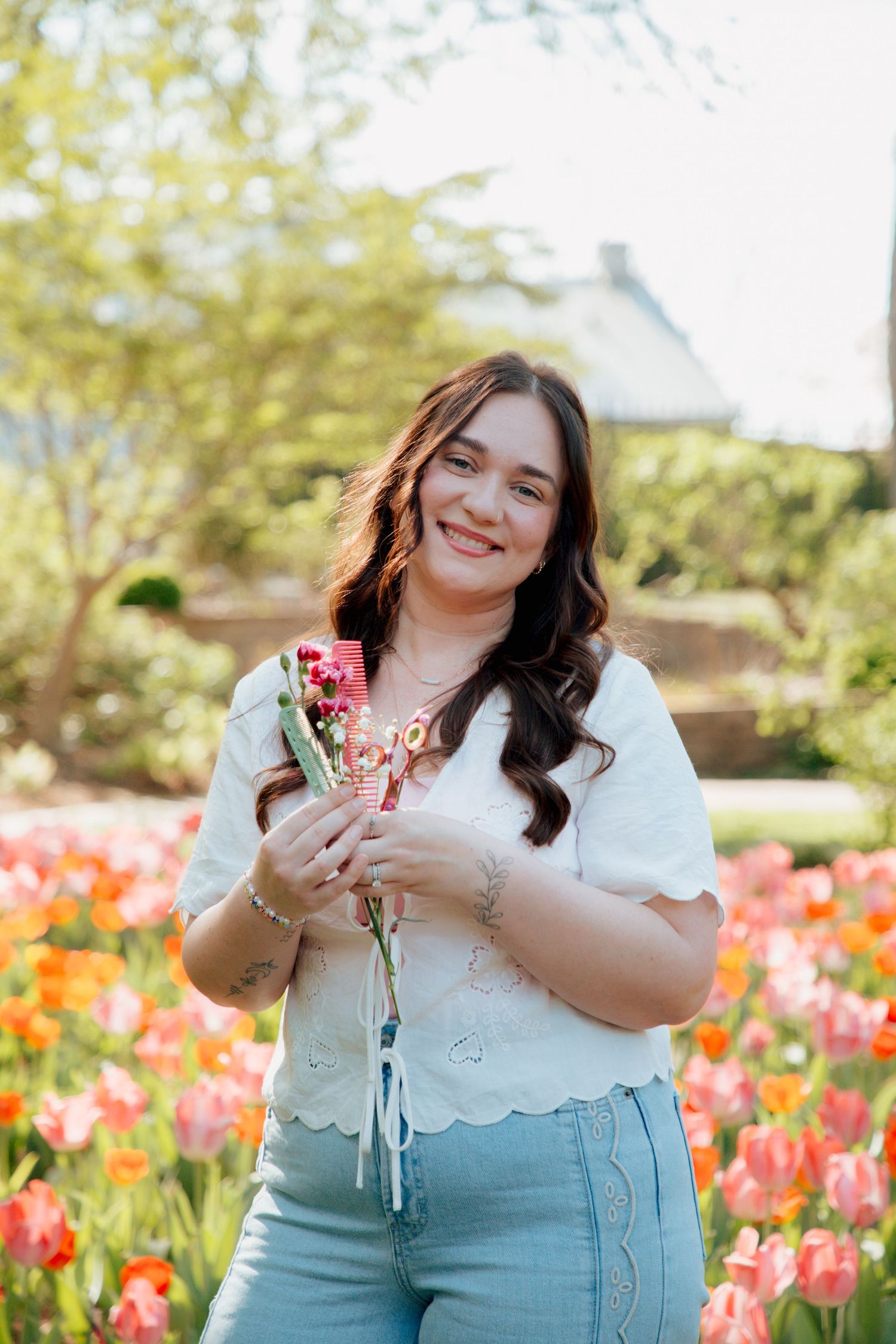 Smiling brunette woman holds pink flowers while standing in vibrant tulip garden on sunny day.