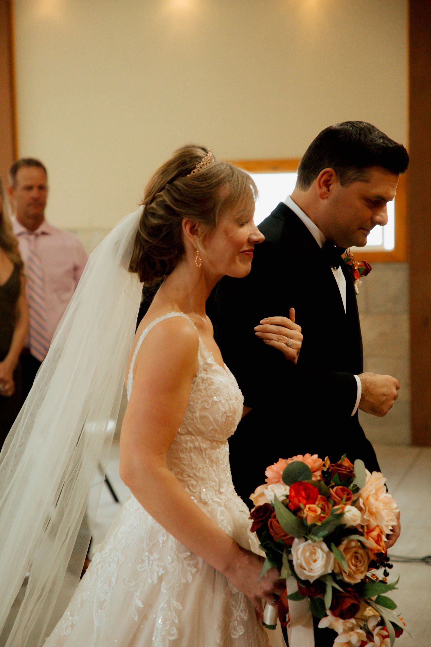 A radiant bride in lace gown holds an autumn bouquet while walking with her groom during the ceremony.