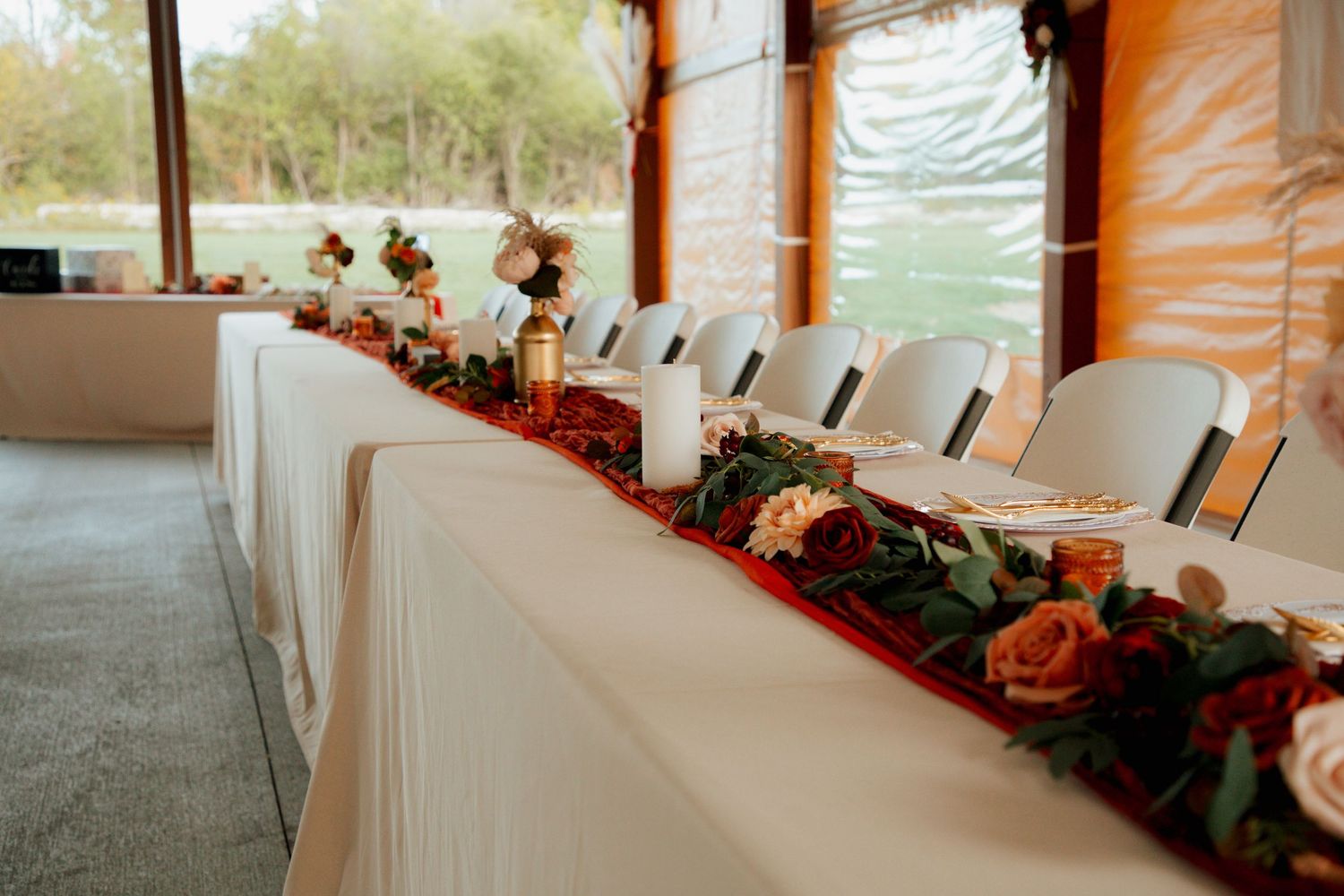 Head table decorated with red floral garland, candles, and roses at wedding reception.