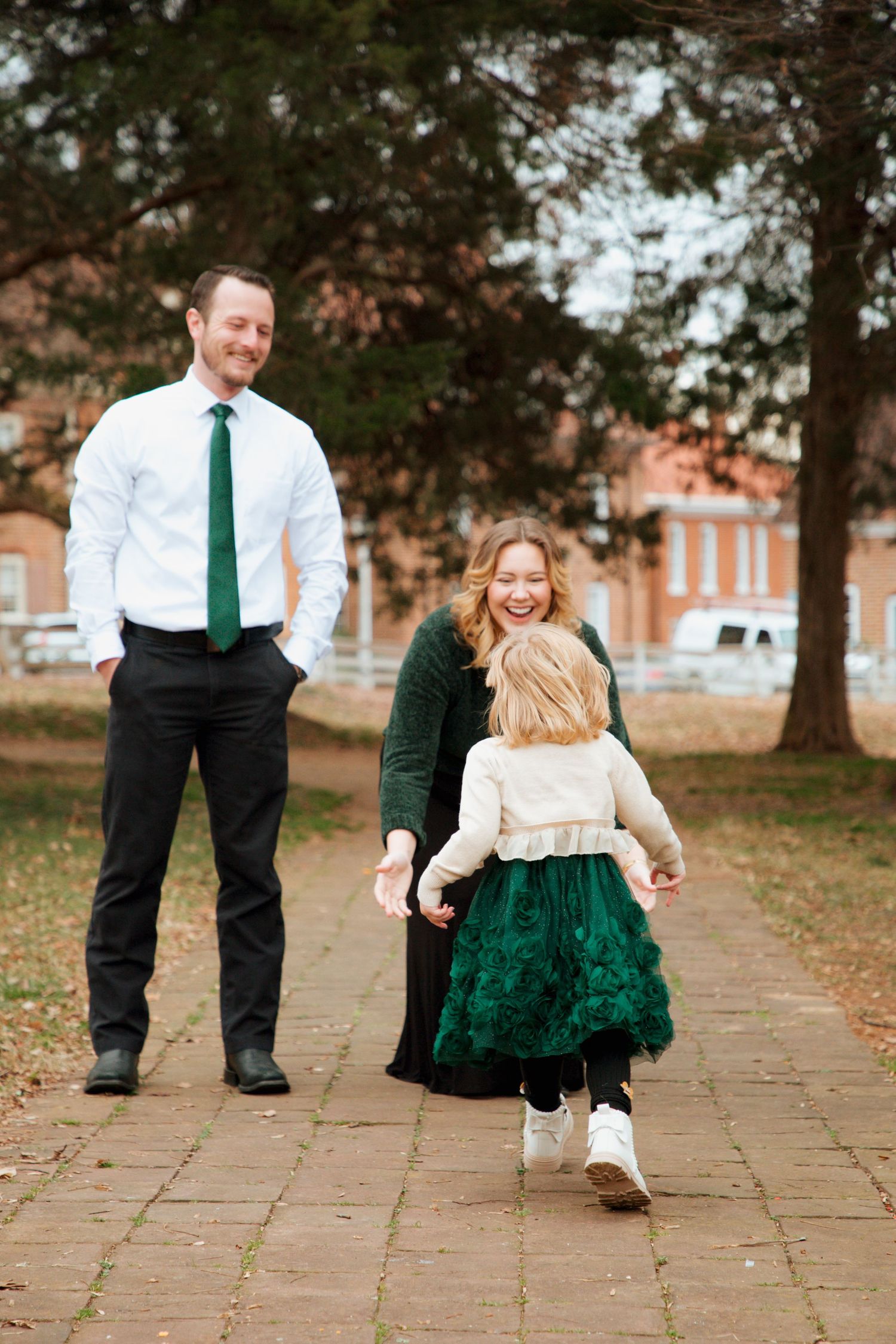 Pregnant mother and father laughing with toddler daughter on brick path during fall family photos.