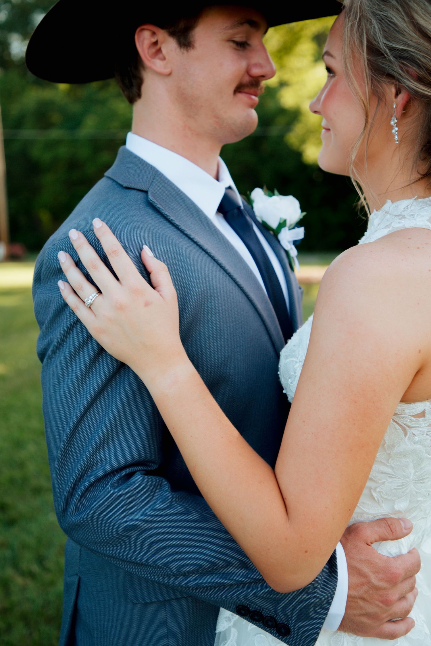 Bride and groom in blue suit and cowboy hat share intimate moment outdoors.