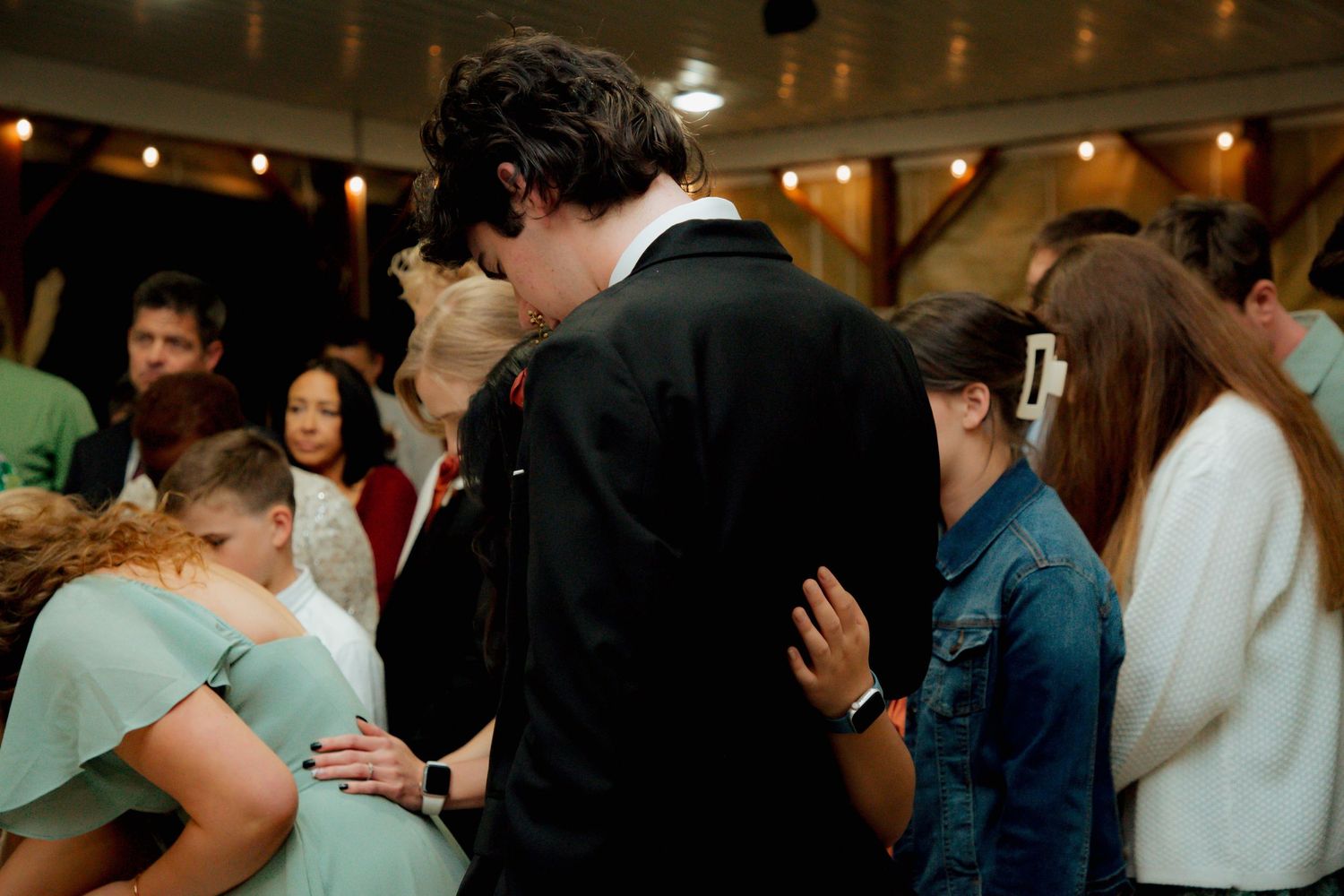 Groom in black tuxedo embraces bridesmaid in mint dress during emotional wedding reception moment.
