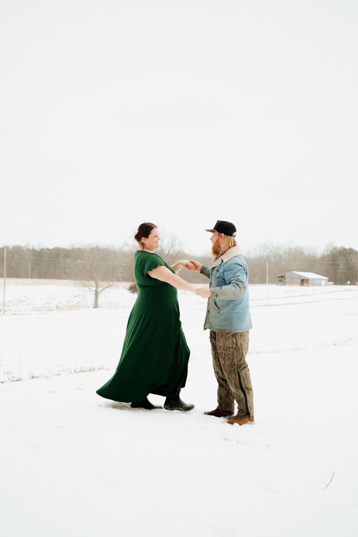 Couple in love dancing together in a snow-covered field, woman in flowing green dress.