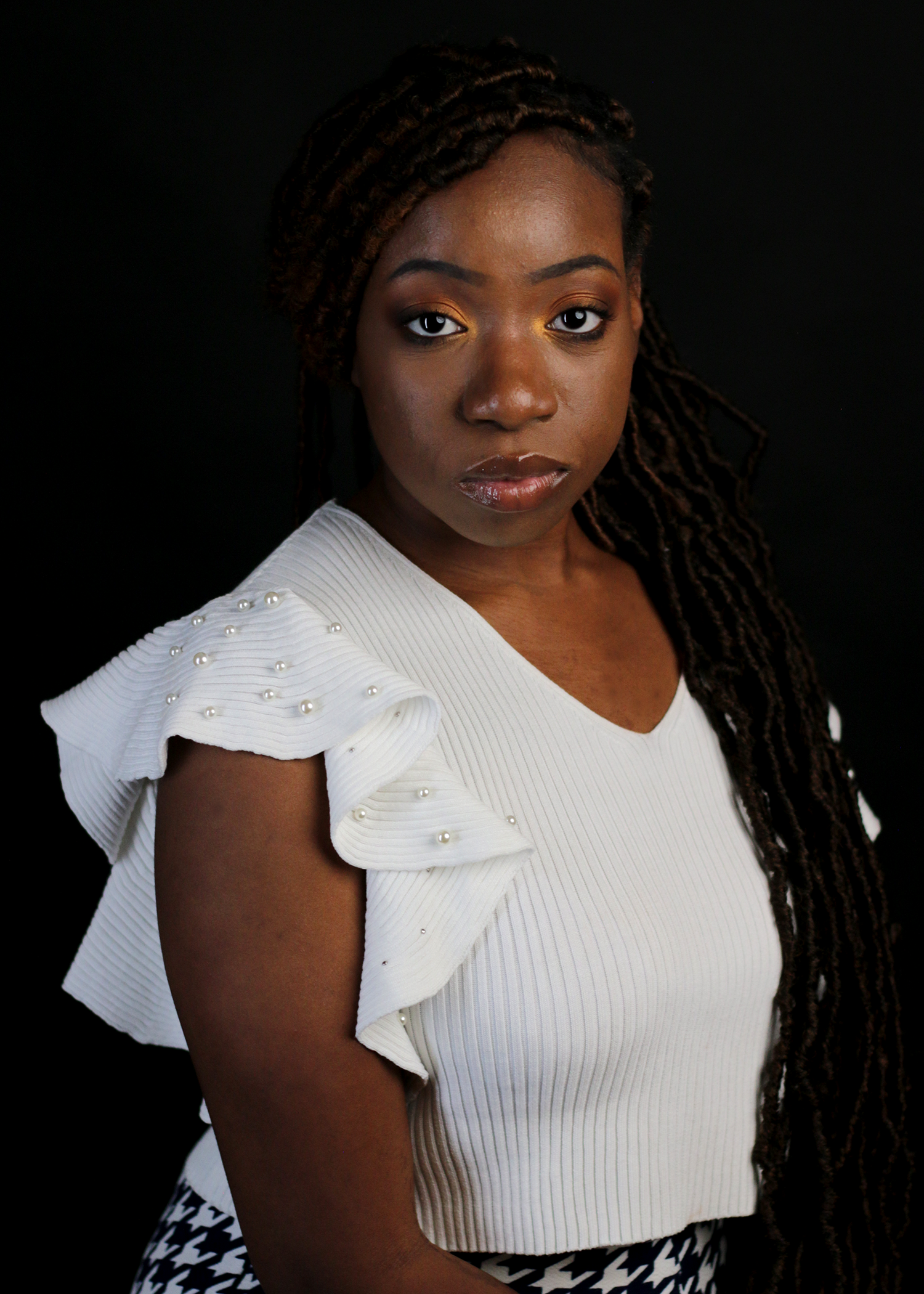 Young Black woman with locs in white ruffled pearl-embellished top poses for portrait.
