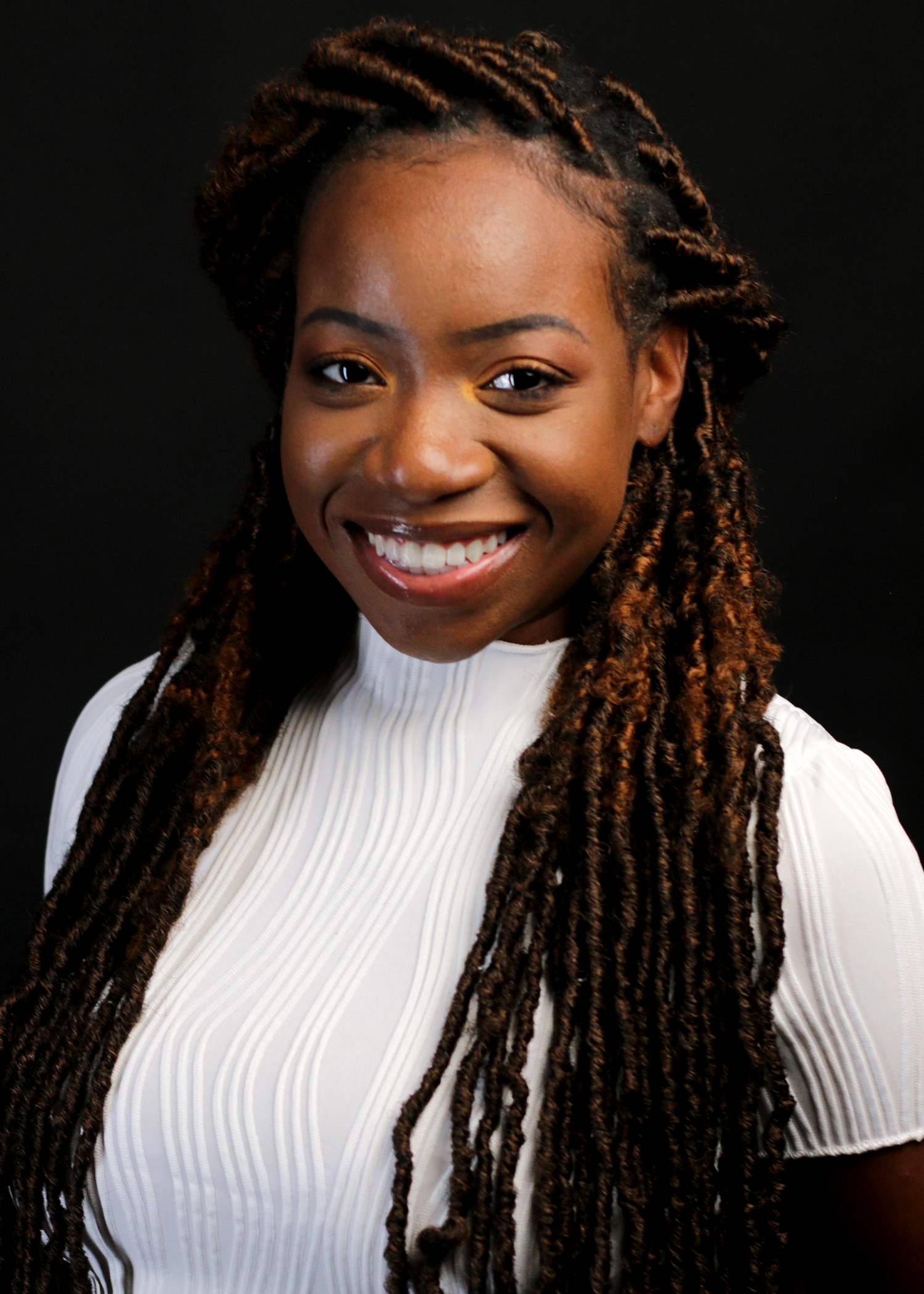 Smiling young Black woman with brown locs wearing white ribbed turtleneck top headshot.