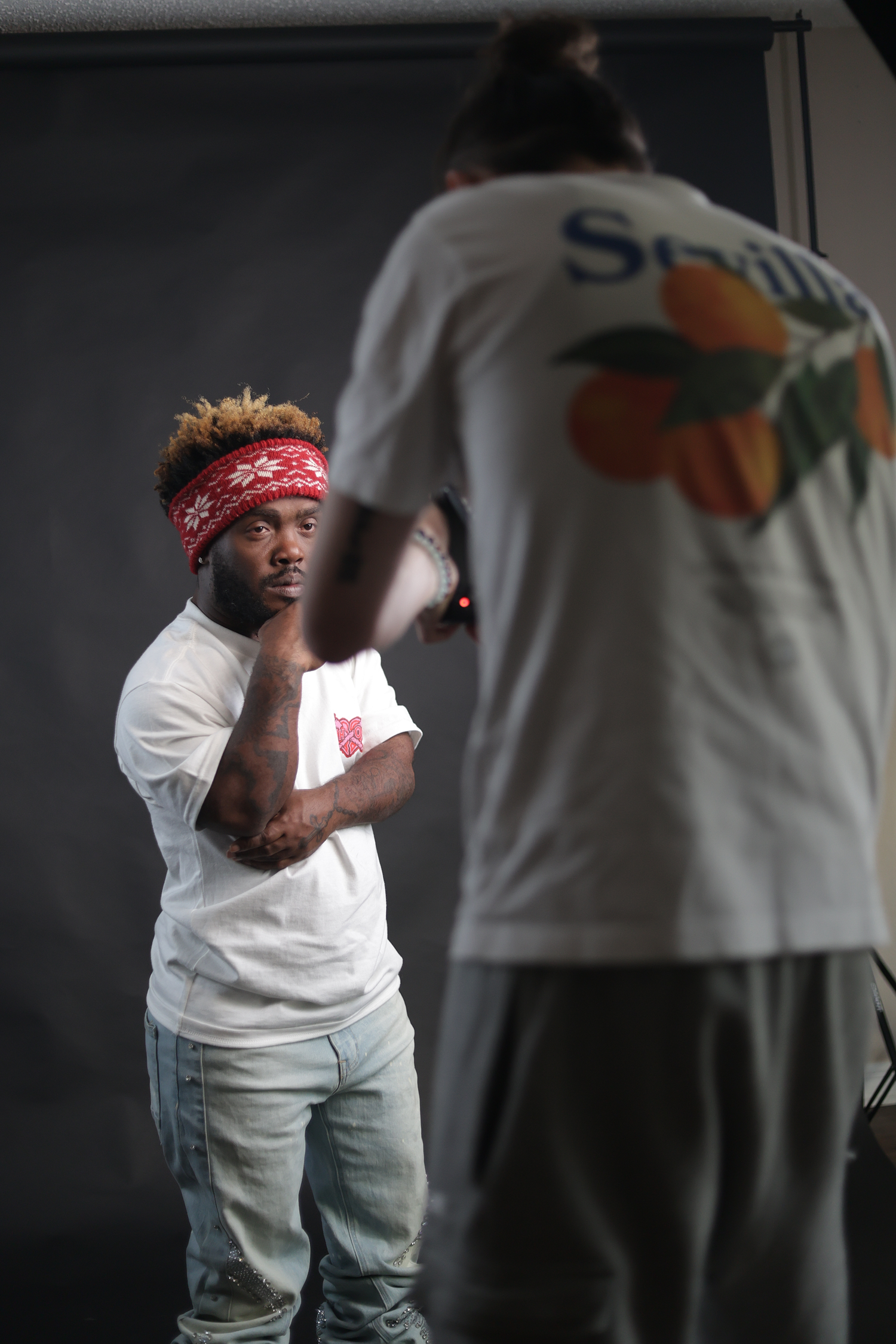 Young man with red bandana headband in white tee stands in photography studio setting.