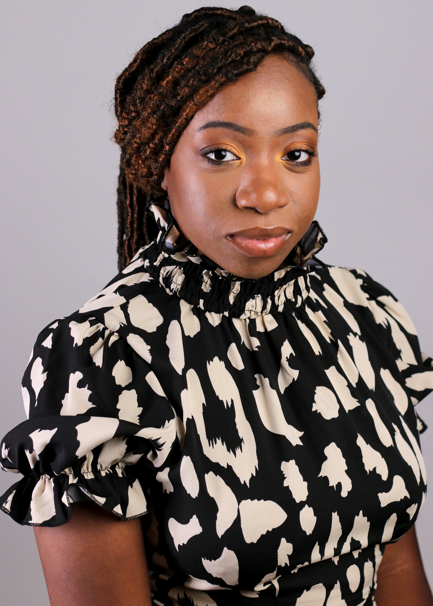 Young Black woman with locs wearing black and white patterned blouse poses for portrait.