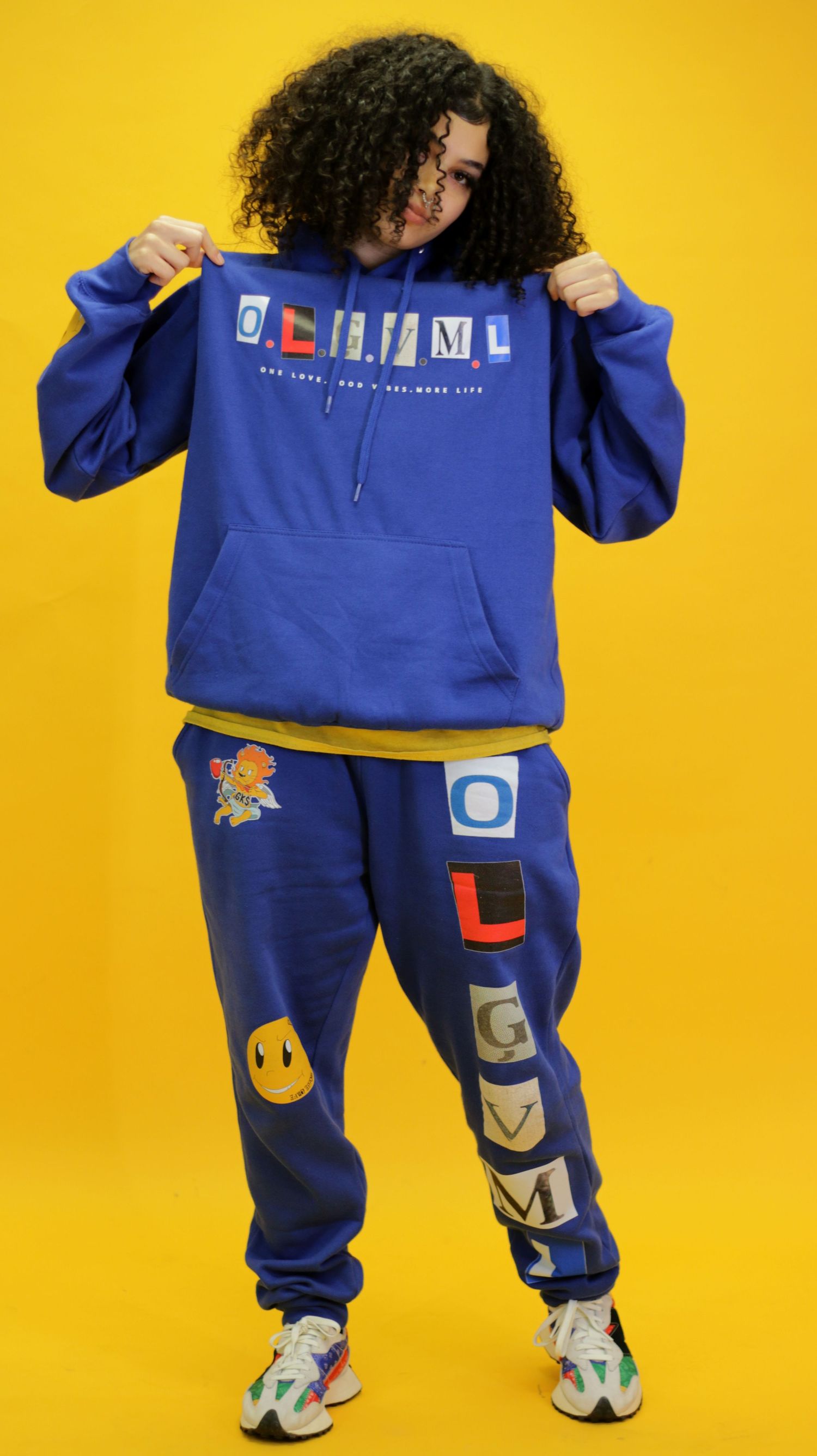 Person in blue OLGVML hoodie and jogger set poses against bright yellow background.