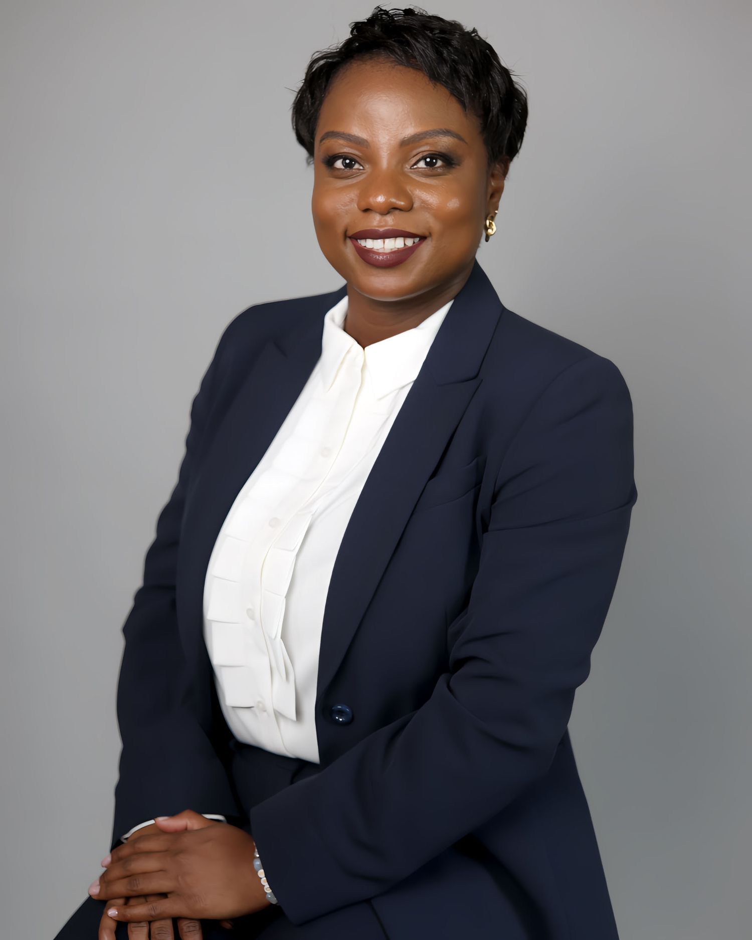 Professional woman in navy blazer and white blouse smiling for a corporate headshot on gray background.