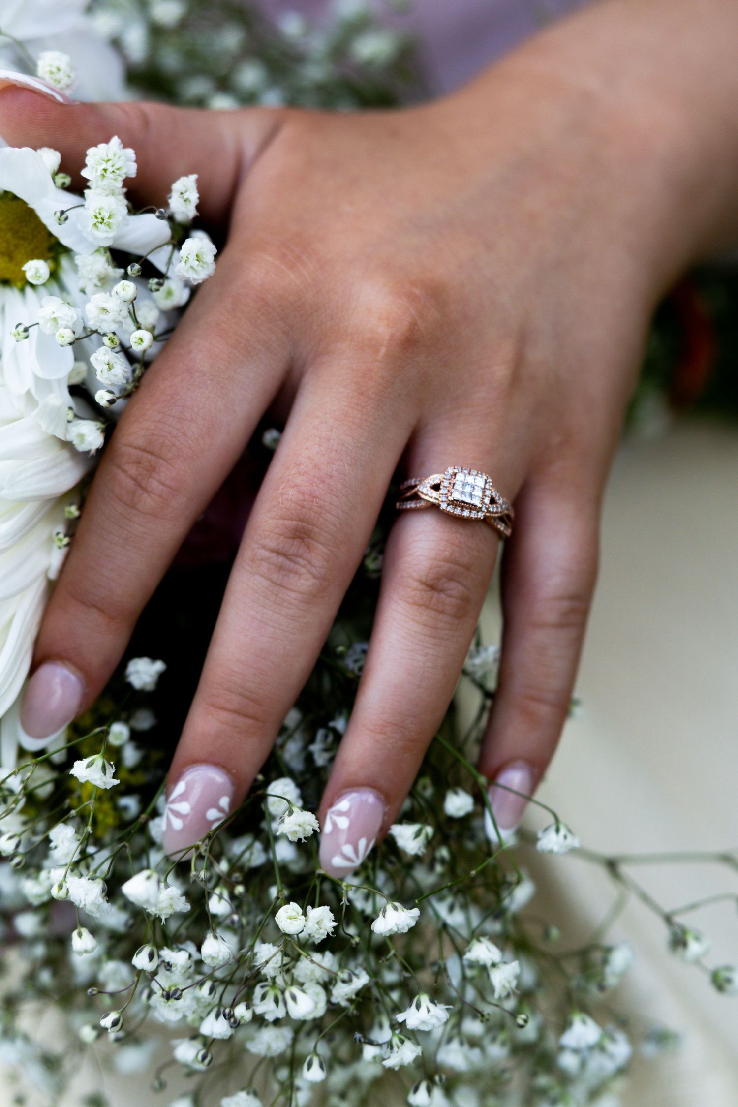 Close-up of a bride's hand wearing a rose gold diamond engagement ring, resting on a white floral bouquet.
