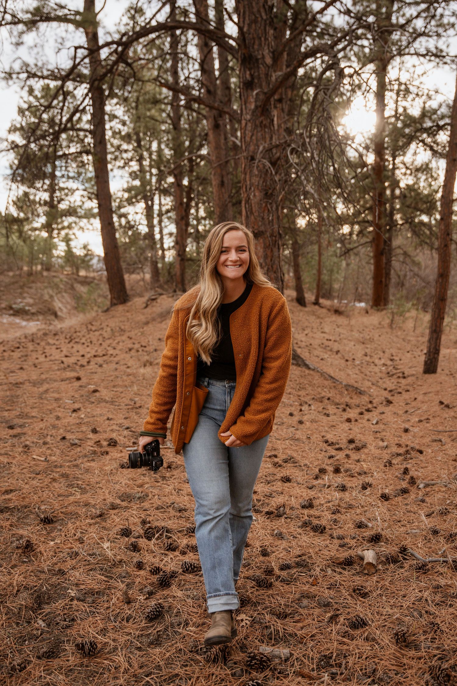 blonde photographer walking through the woods with camera in their hand
