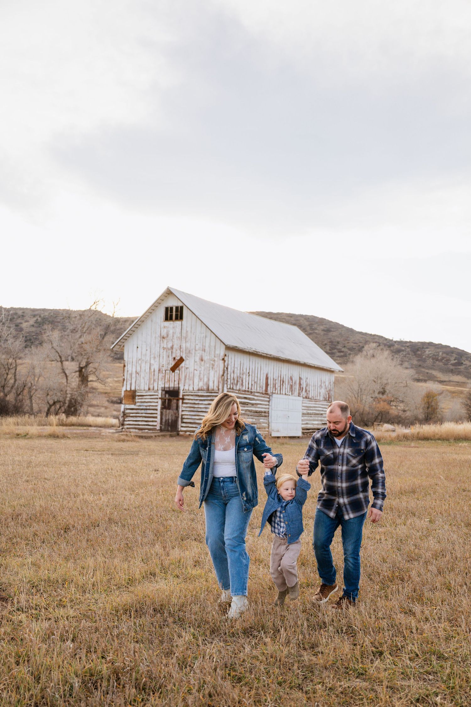 People walking and laughing together in a rustic field with white barns and mountains in the background.