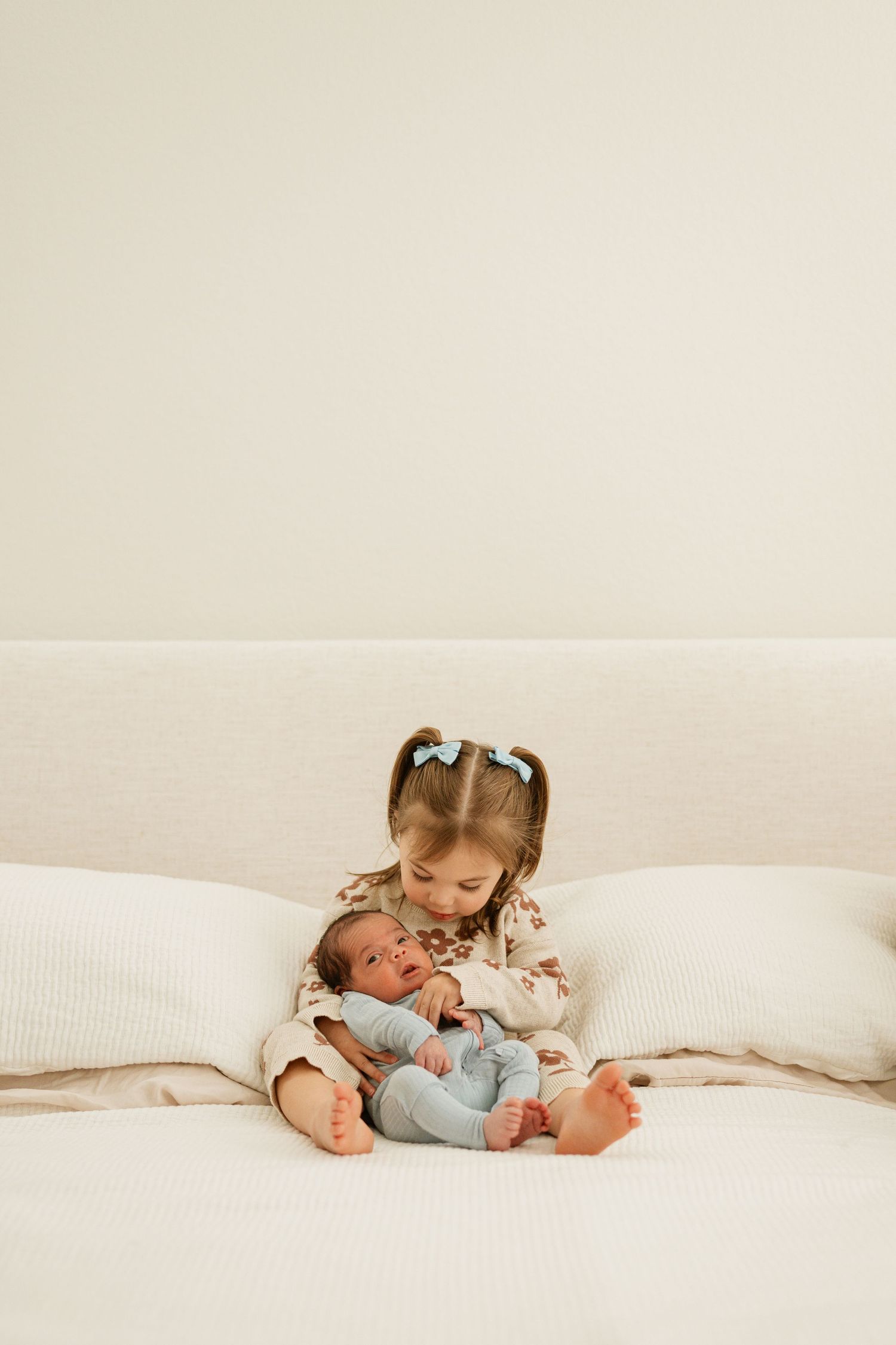 Two children in white bedding share a sweet moment together while lying on a bed.
