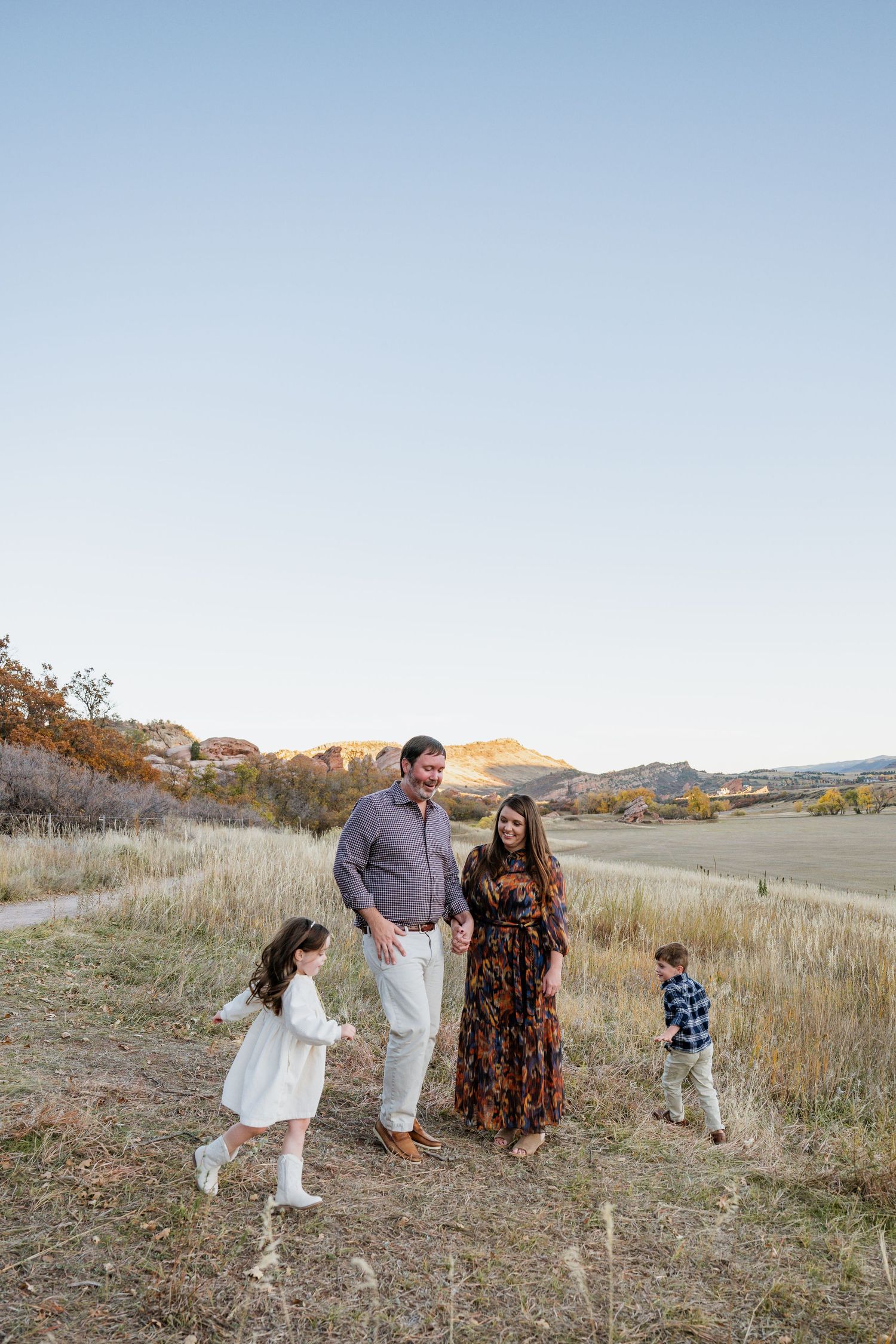 Family walking together through a scenic autumn field with golden grass and rolling hills in the background.