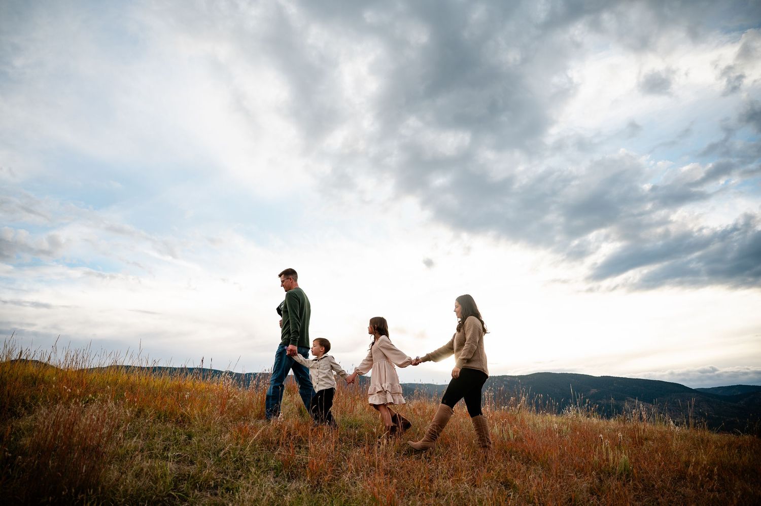 Silhouettes of people walking along a hilltop against dramatic cloudy sky at sunset.