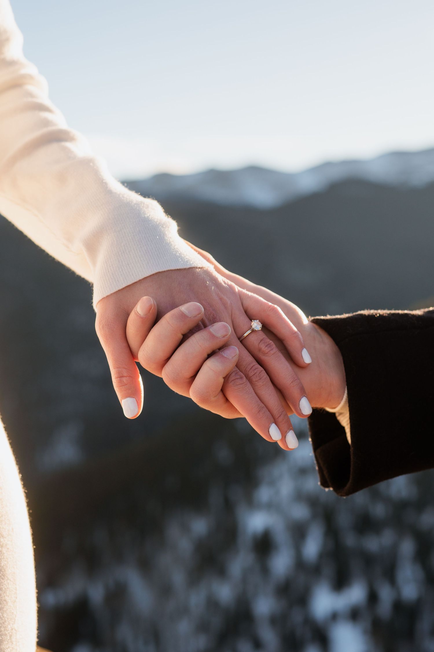 An engaged couple stands on a cliff in Evergreen, Colorado, with majestic mountains as the perfect backdrop, capturing their love and advent